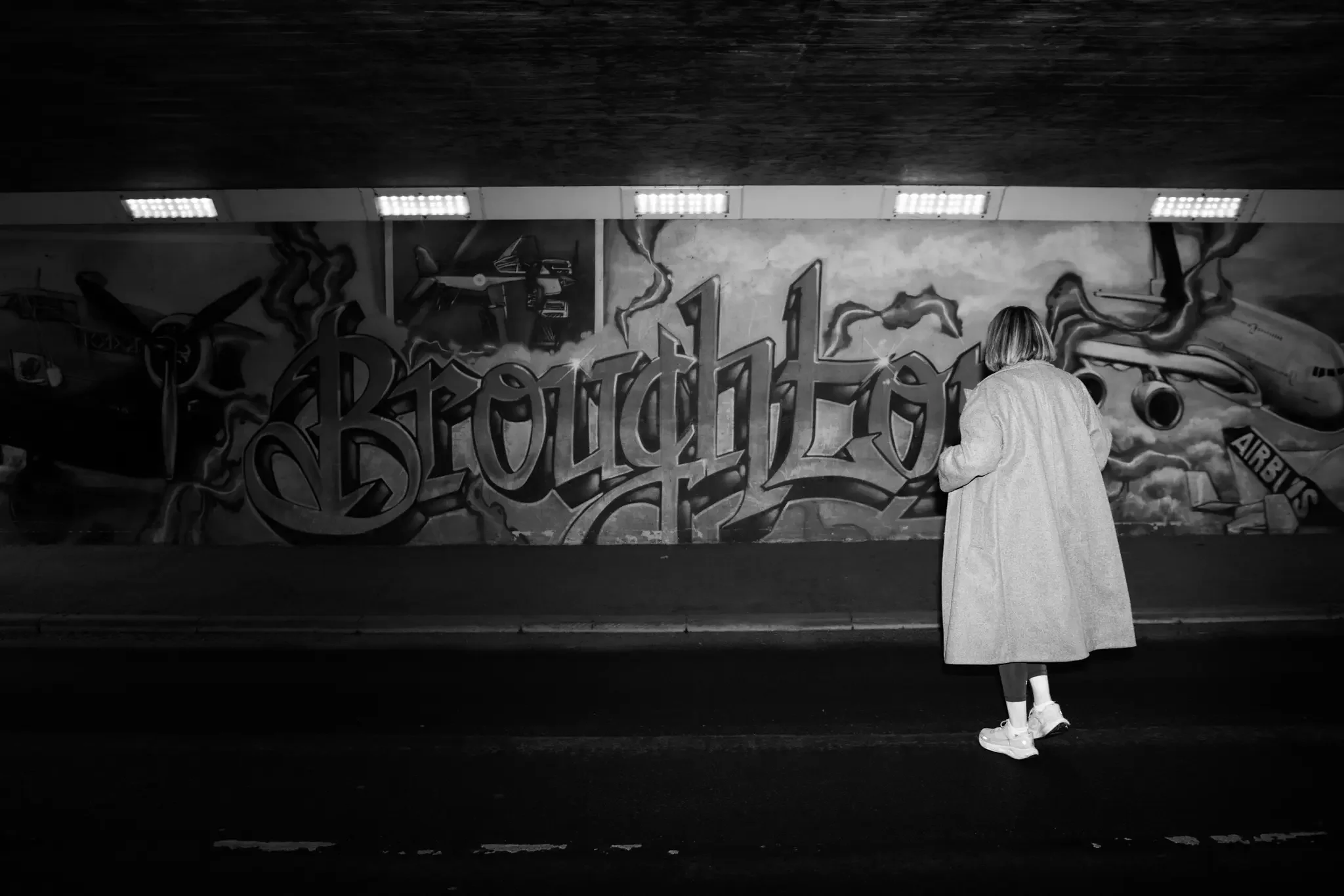 A woman walking past graffiti art with the words 'Brought Love' under an overpass, in black and white.