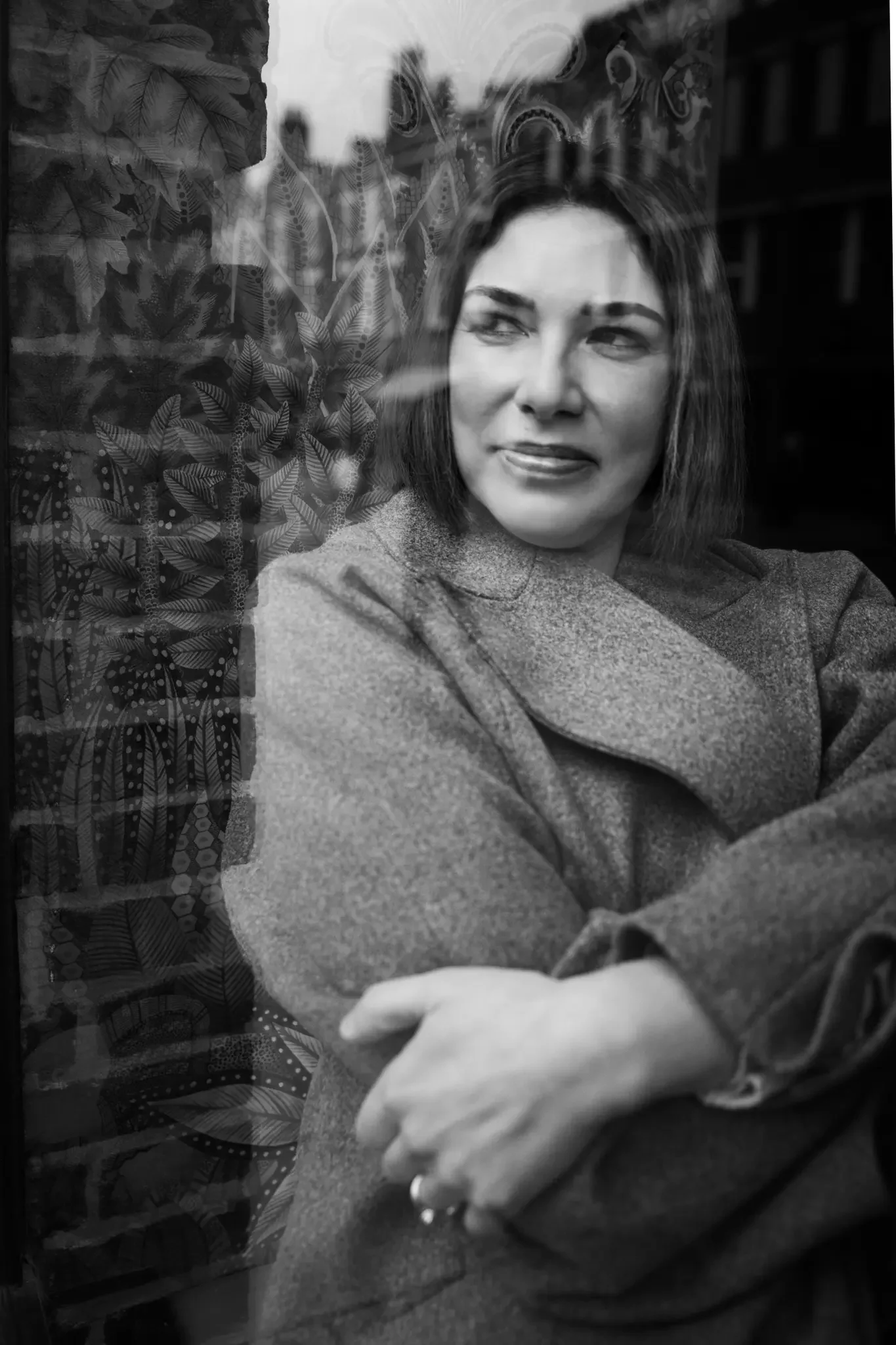 A woman with short hair sitting next to a window with a potted plant behind her, looking away thoughtfully.