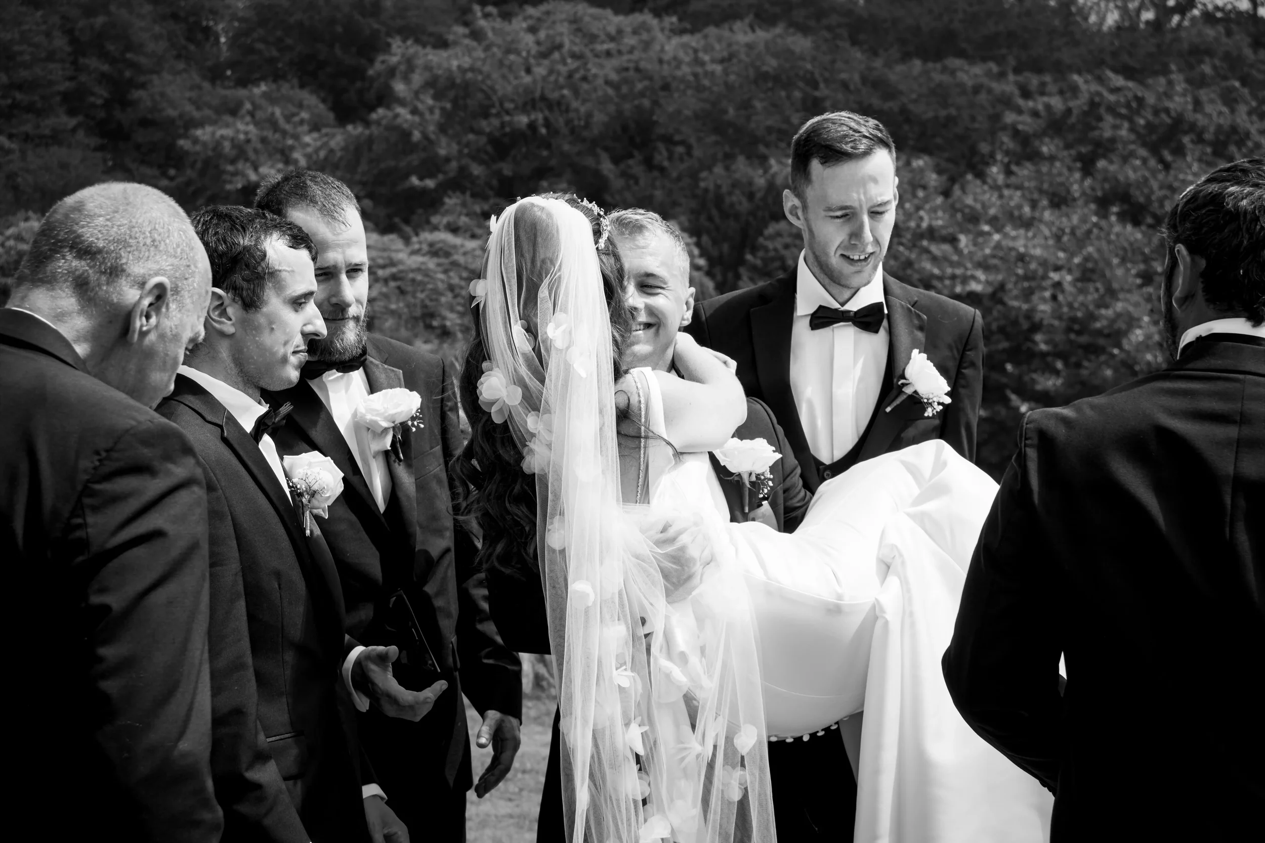 groom-picks-up-bride-surrounded-by-groomsmen-talhenbont-hall-wedding.webp