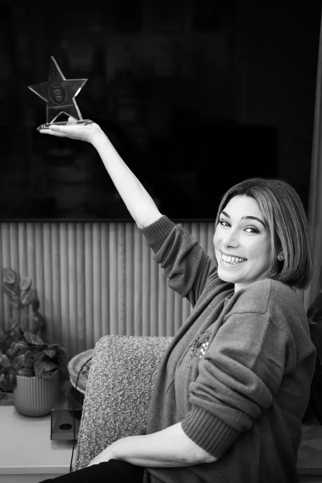 A smiling woman in casual clothing holding a star-shaped award or trophy above her head.