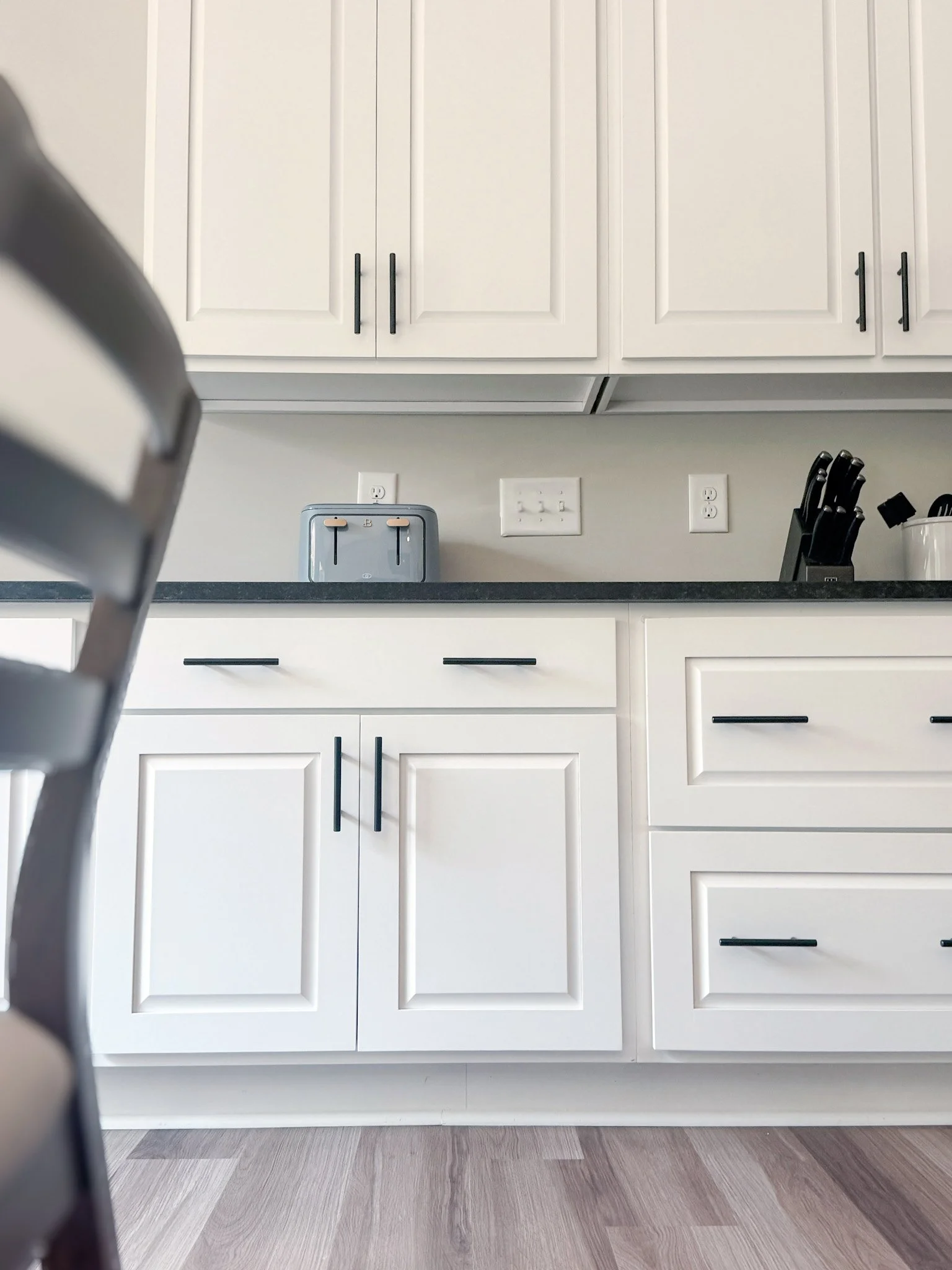 These “Dawson” style cabinets feature clean, structured lines that bring a timeless appeal, while the black honed countertops introduce a subtle contrast that elevates the overall space. 