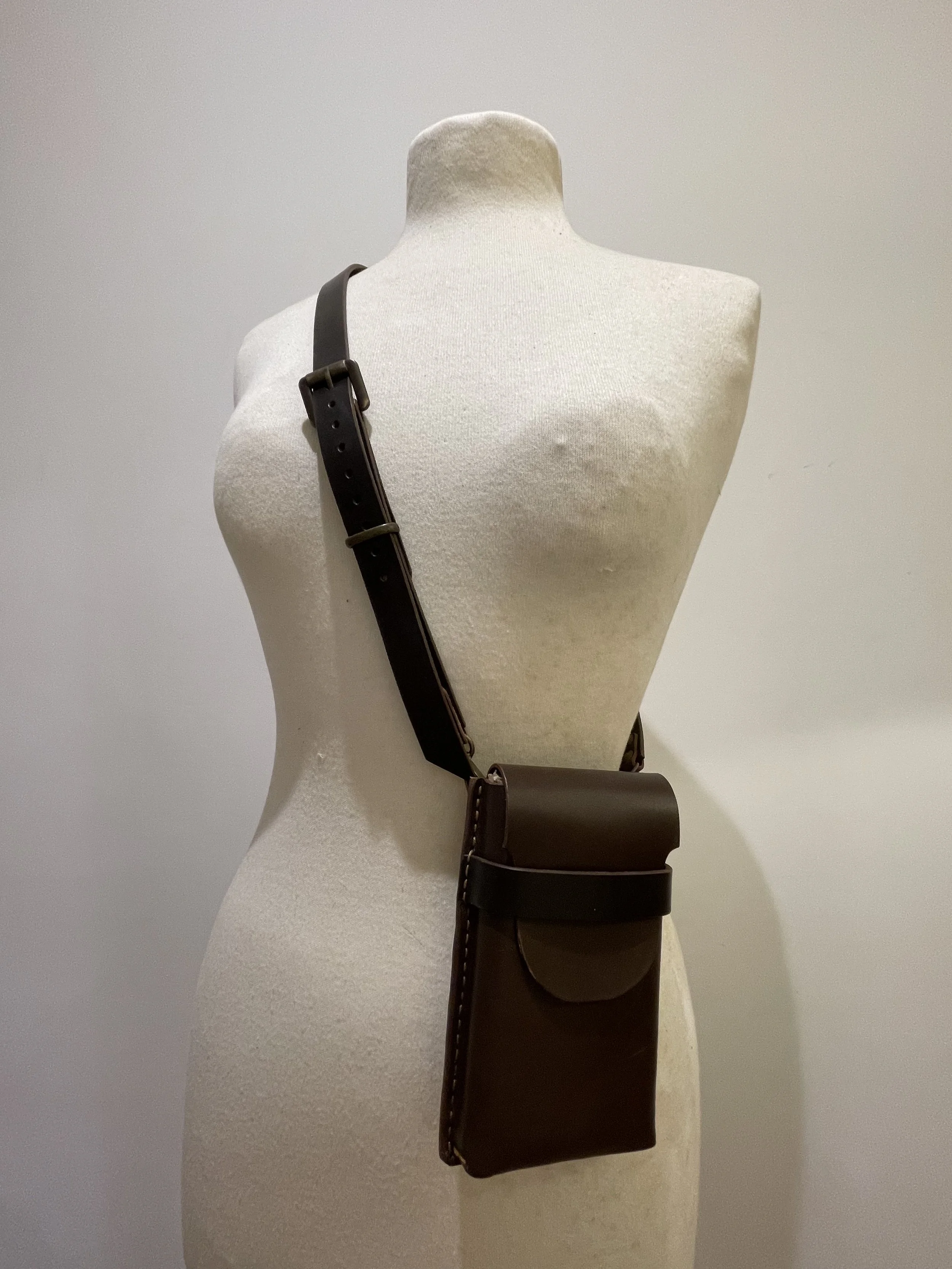 A beige mannequin torso with a black leather shoulder bag and a wider strap hanging diagonally across the front.