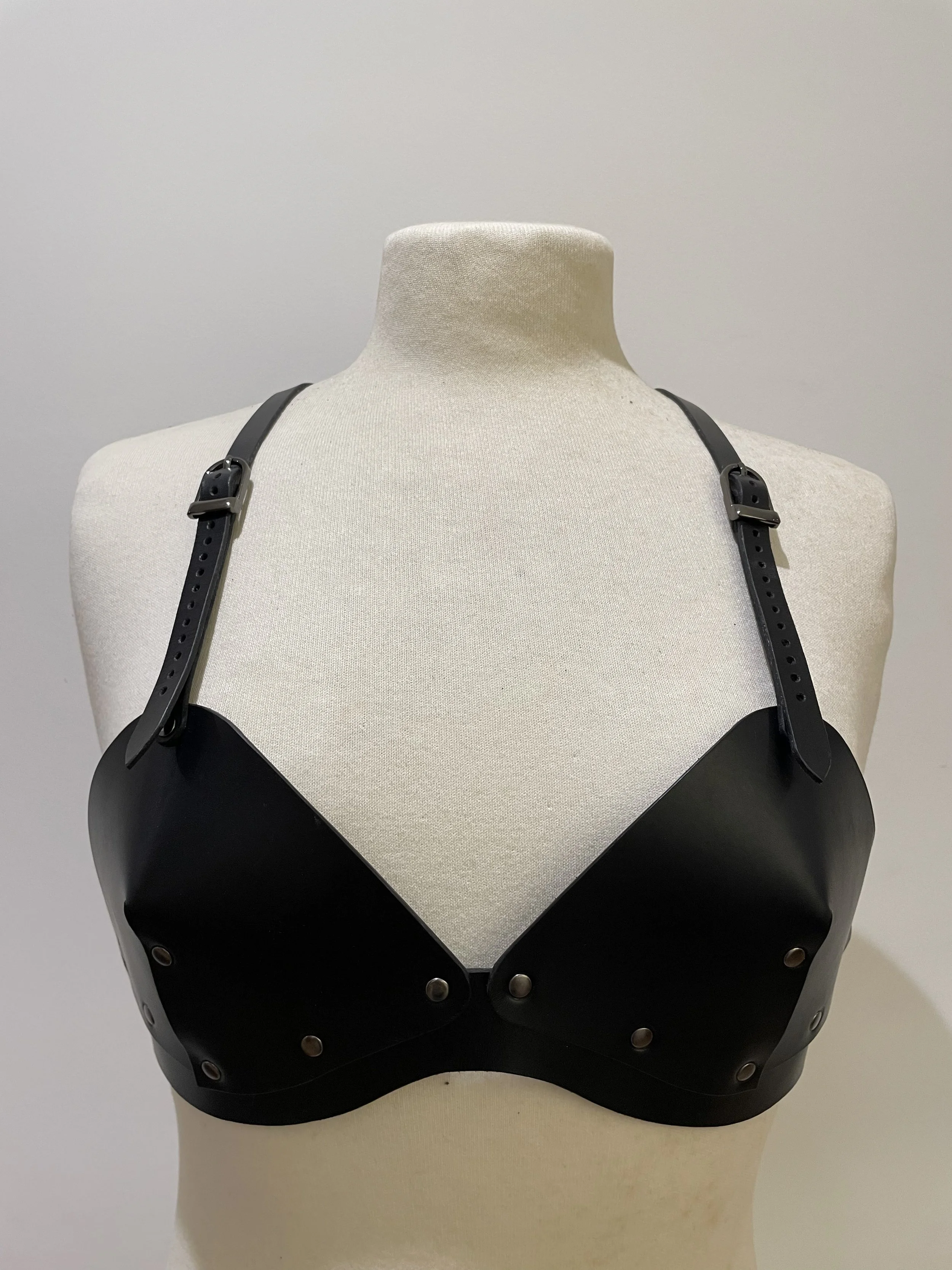 Black leather harness with adjustable straps and silver hardware on a beige mannequin bust.