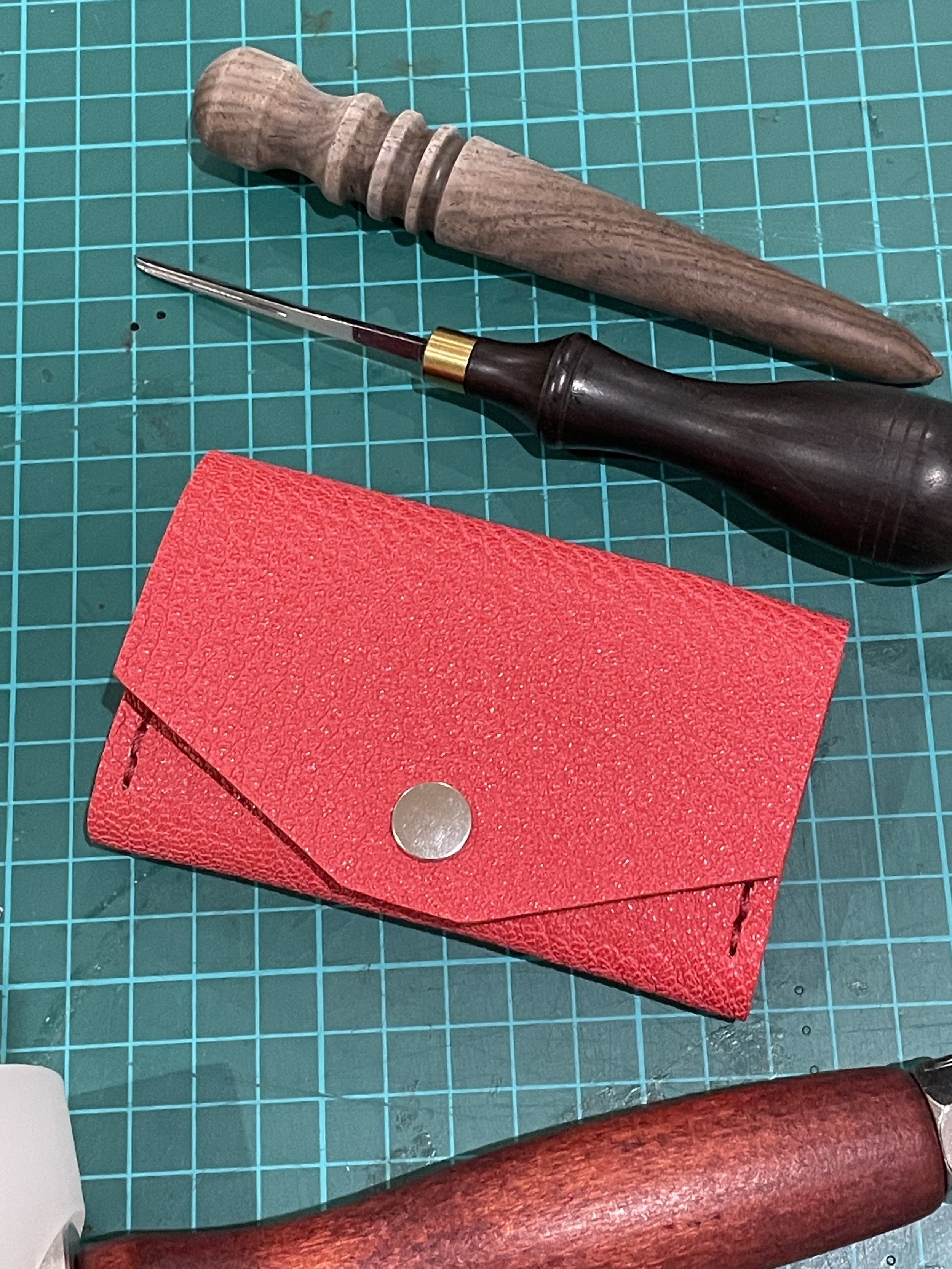 A cutting mat with a wooden handle tool, a small red cloth, and a black screwdriver with a curved tip on top.