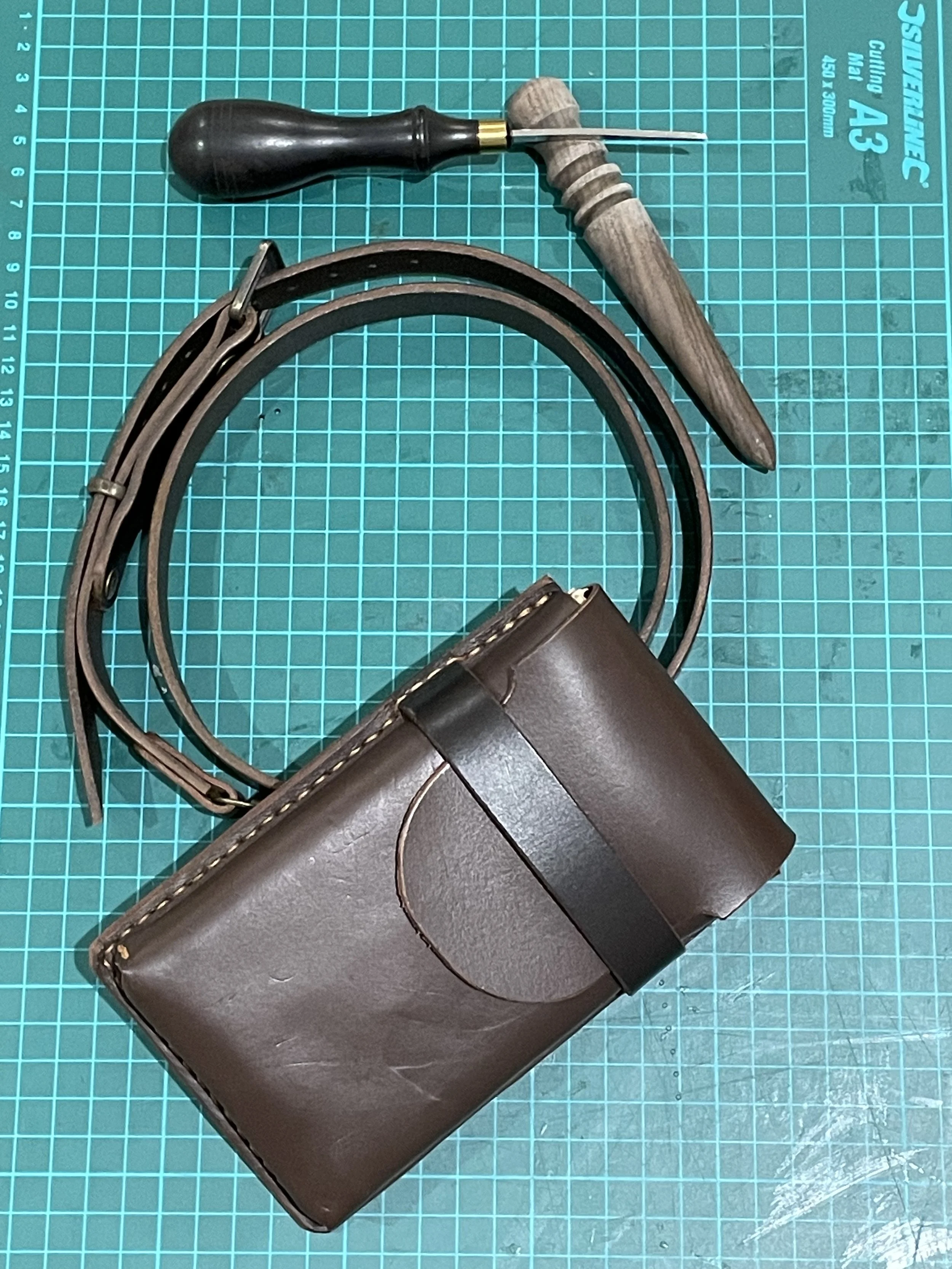 A leather or faux leather holster with a belt and a screwdrivers placed on top on a green cutting mat.