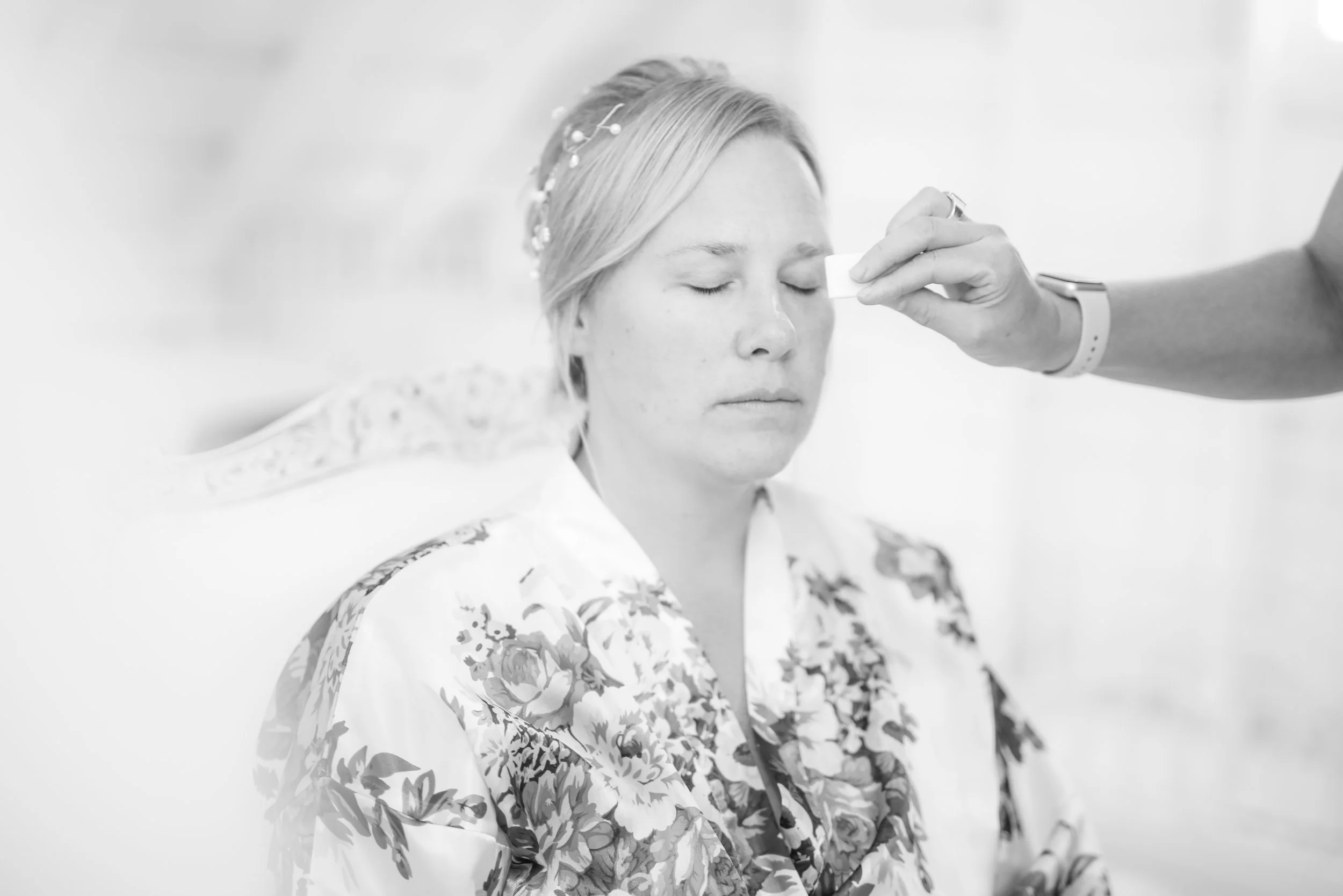 A bride with closed eyes sitting calmly as someone applies makeup or skincare to her face, in a bright room, Minnesota based photographer, LKW Photography, photographs