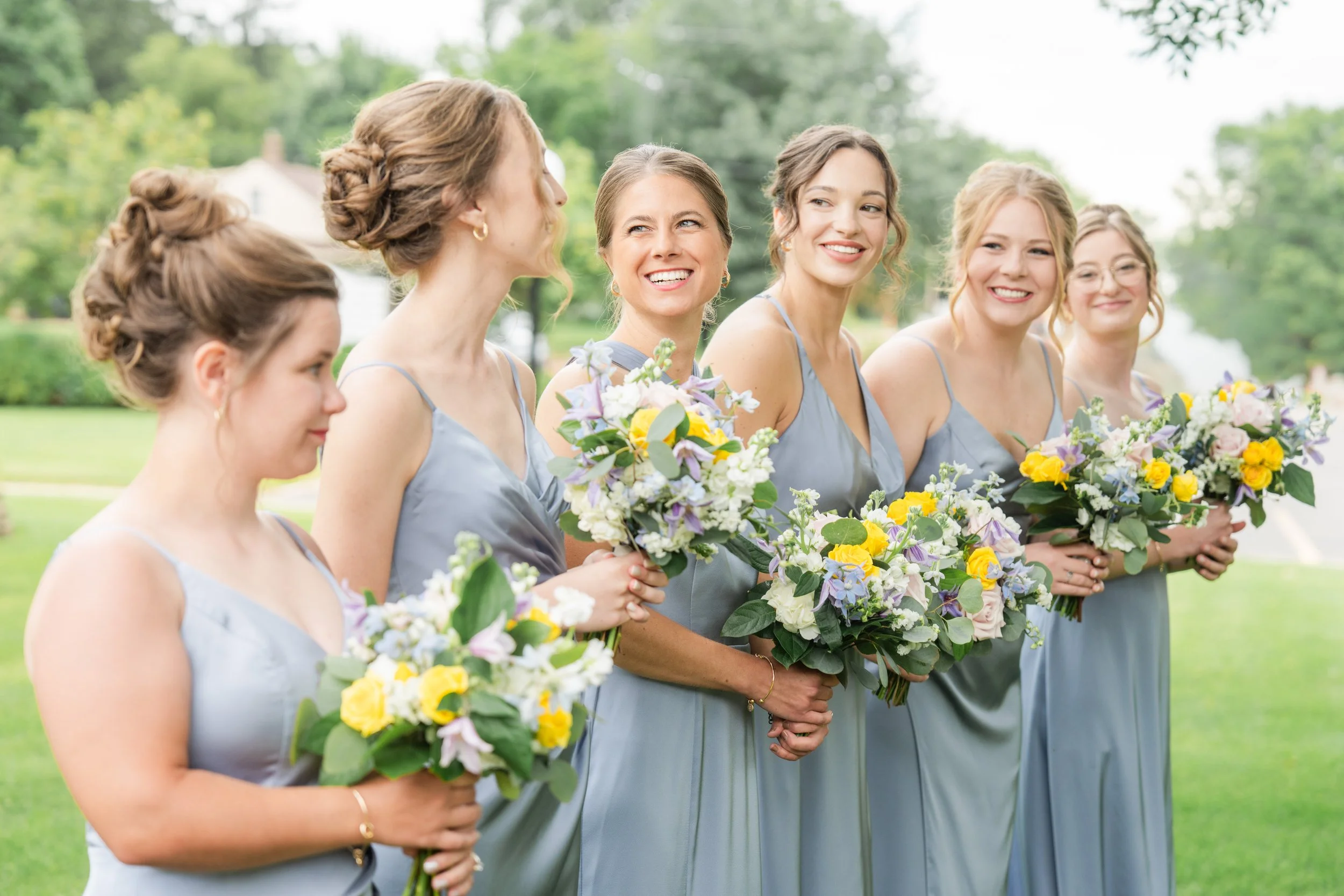 Six bridesmaids in matching light blue dresses holding bouquets of flowers standing outdoors during a wedding, photographed by Minnesota based wedding photographer, LKW Photography.