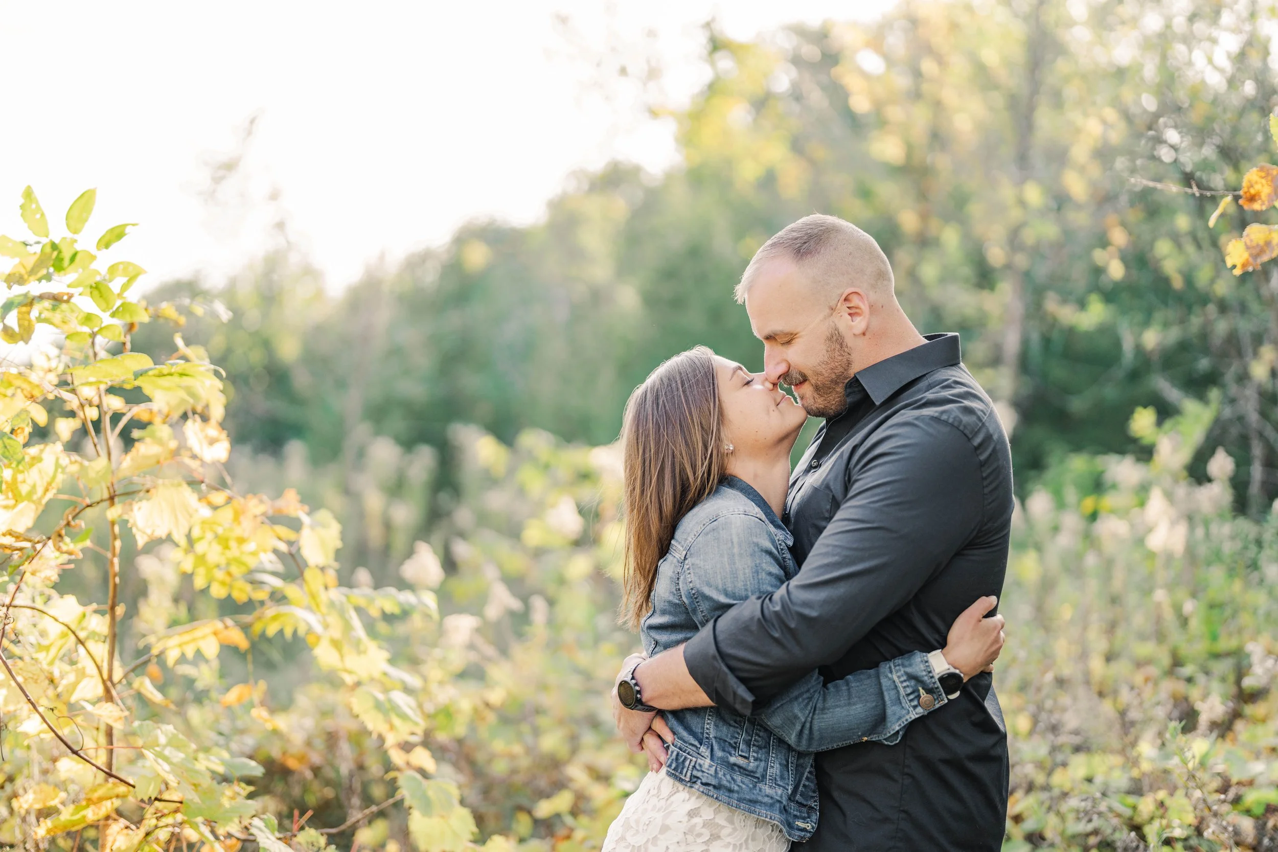 Minnesota wedding photographer, LKW Photography, photographs engagement pictures for a couple hugging in a natural outdoor setting with trees and foliage.