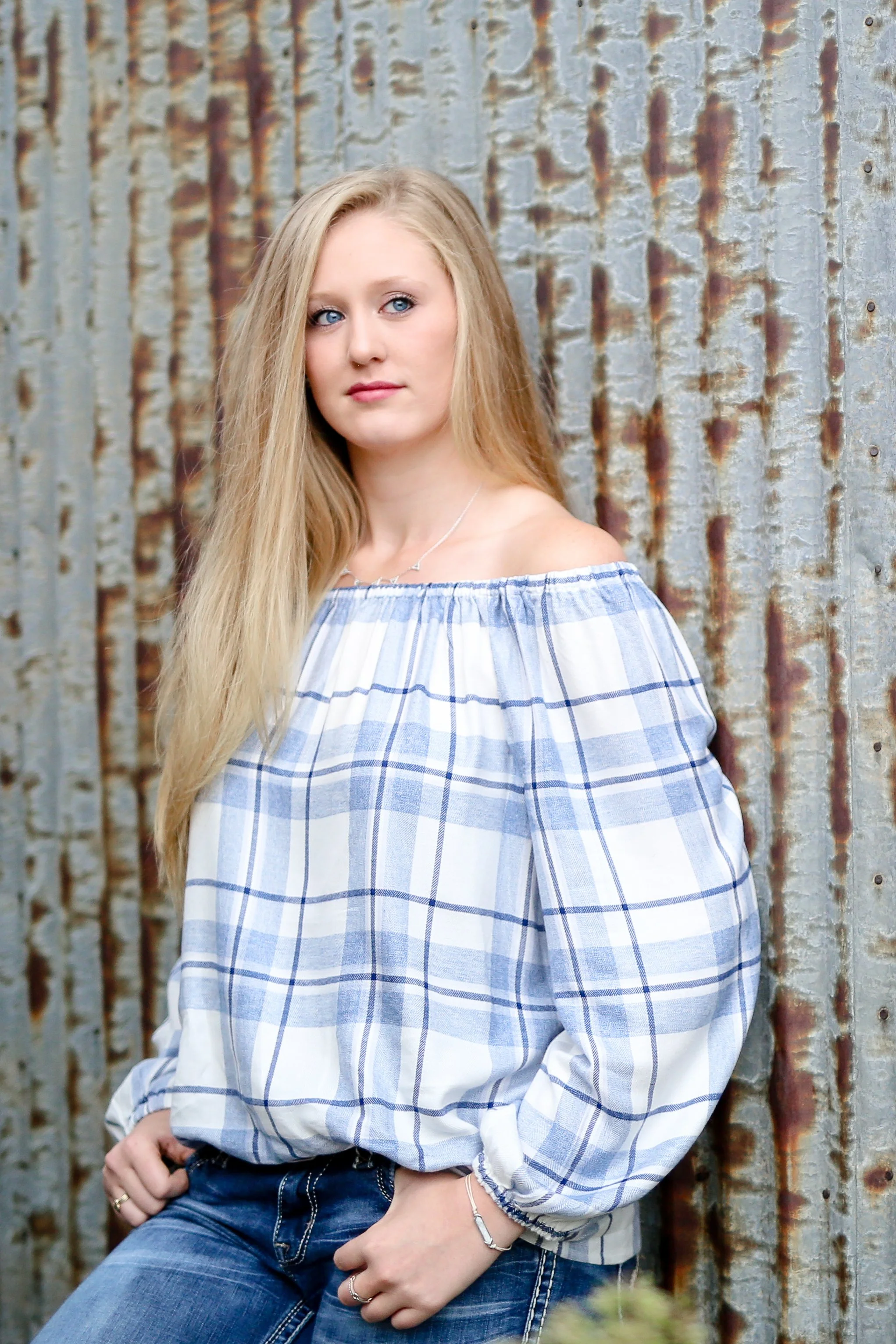 Minnesota senior photographer, LKW Photography, photographs a high school senior with long blonde hair, blue eyes, and fair skin stands in front of a rusty corrugated metal wall with  a relaxed pose.