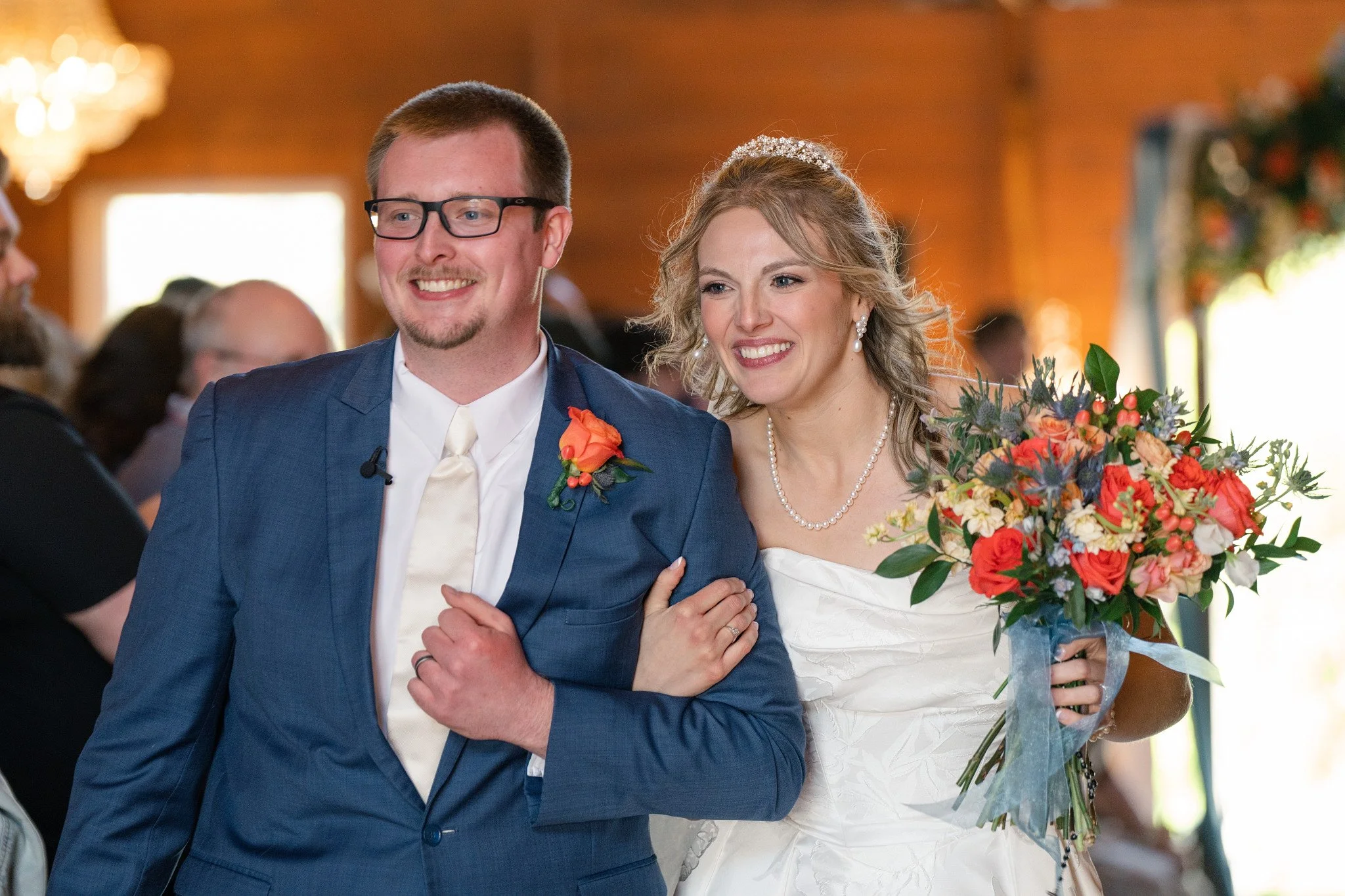 A bride and groom walking down the aisle together on their wedding day, smiling happily. The bride is holding a bouquet of colorful flowers.