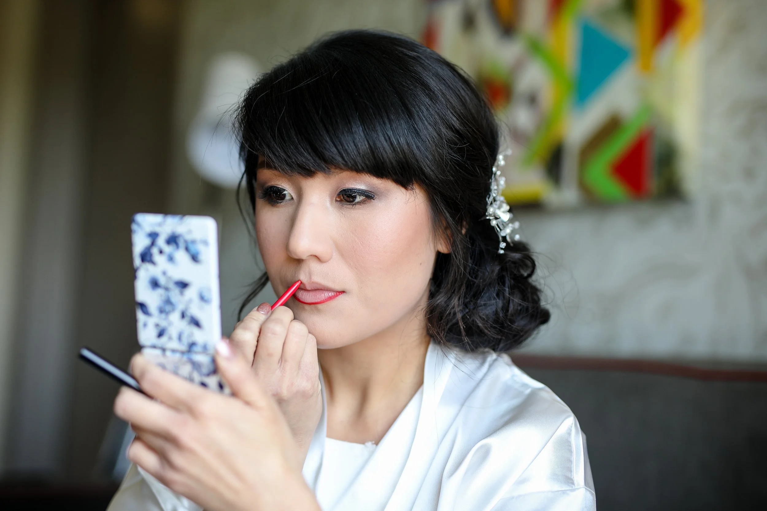 Asian bride applying lipstick while looking in a mirror, taken by MN photographer LKW Photography.