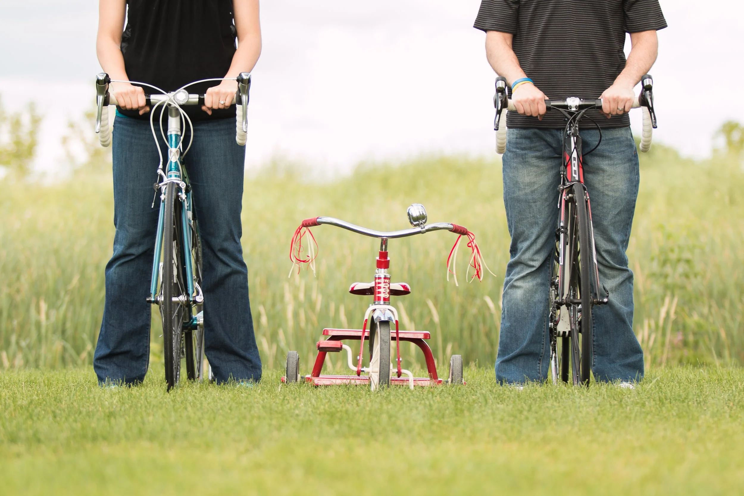 A cute baby announcement with a couple and their bikes, with a trike in between them.  Taken by Minnesota Photographer, Leah Welch of LKW Photography. 