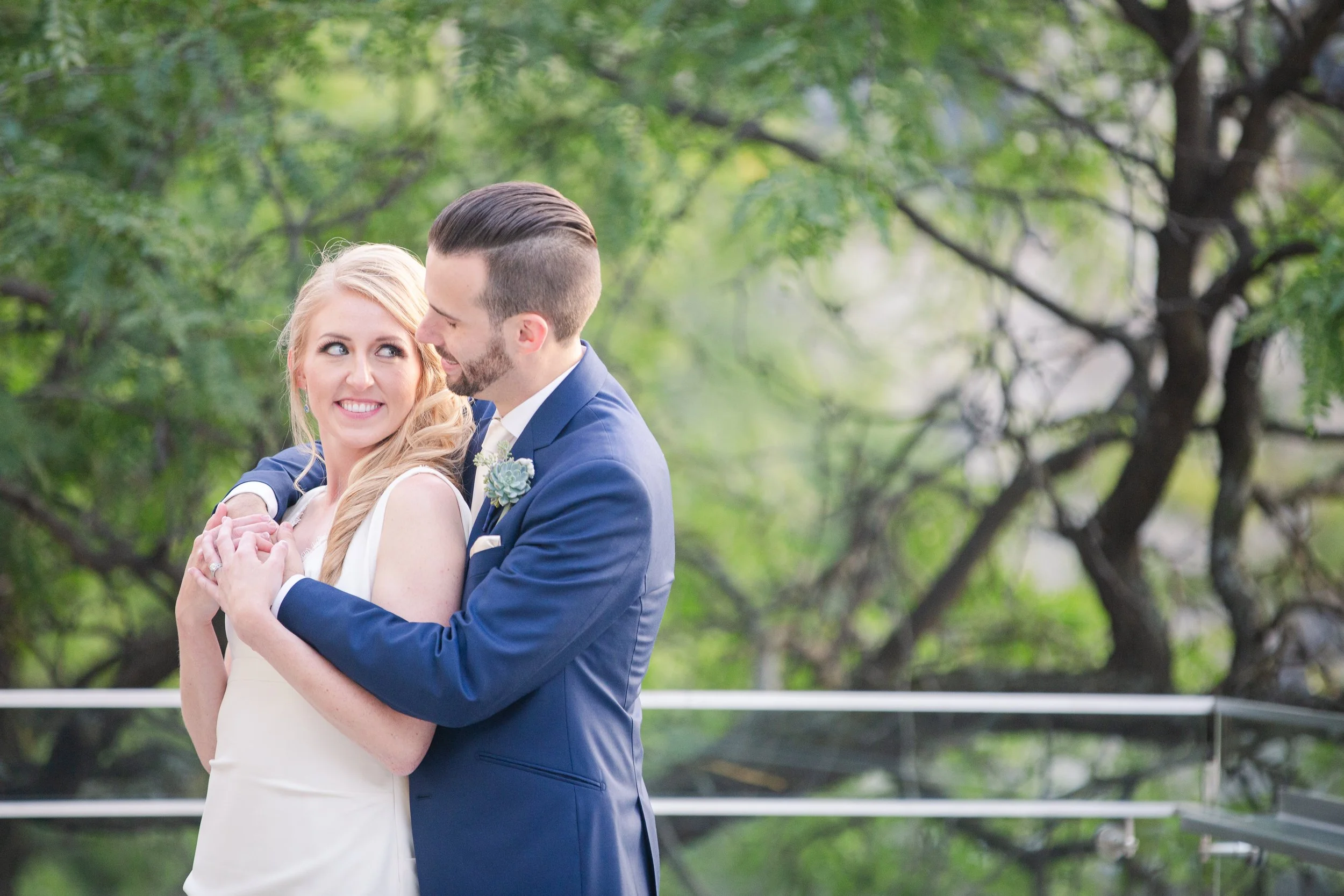 Minnesota based photographer, LKW Photography, photographs a  bride and groom embracing outdoors, smiling at each other amidst green trees.