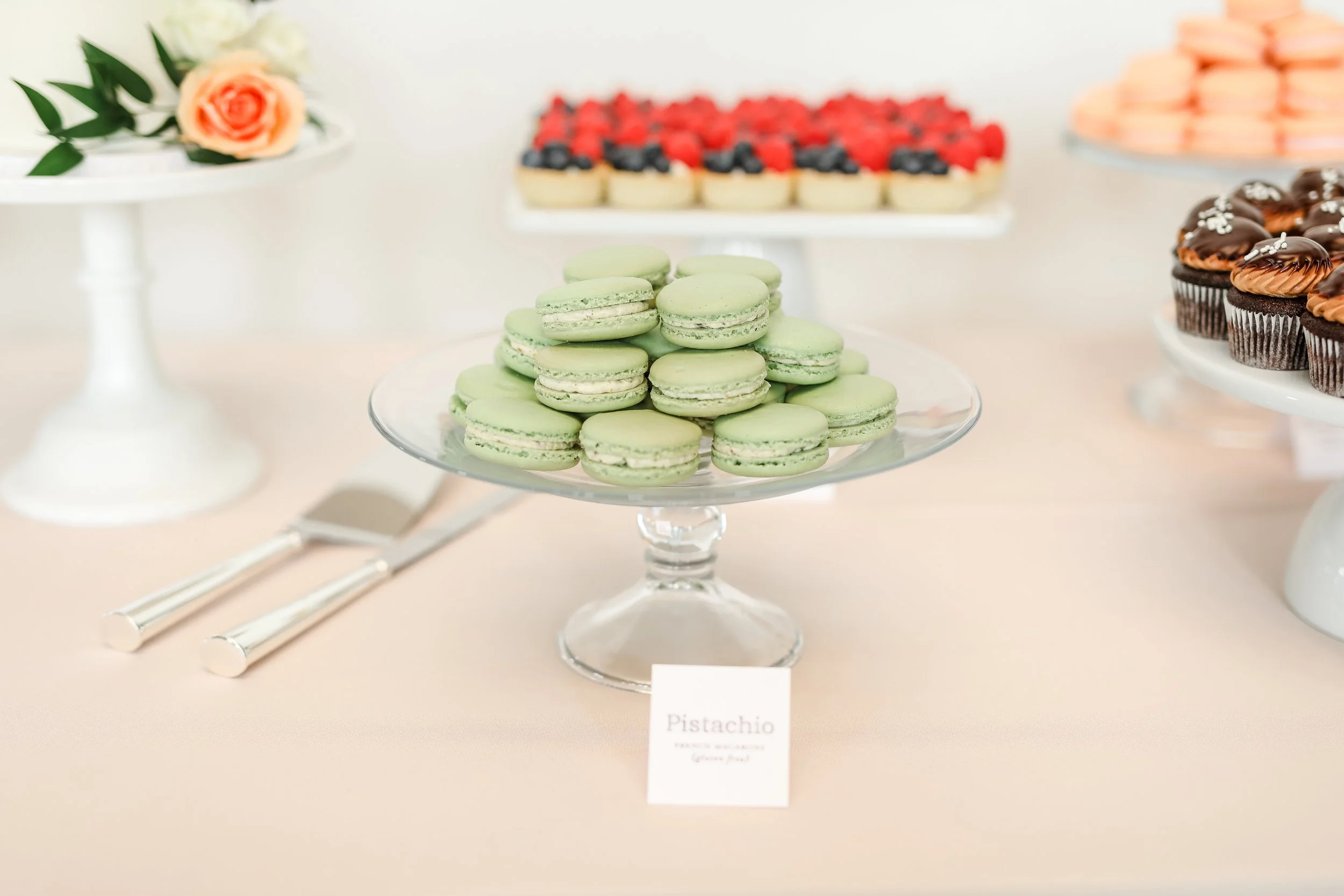 Green pistachio macarons on a glass cake stand at a dessert buffet, taken by Minnesota Wedding Photographer LKW Photography.