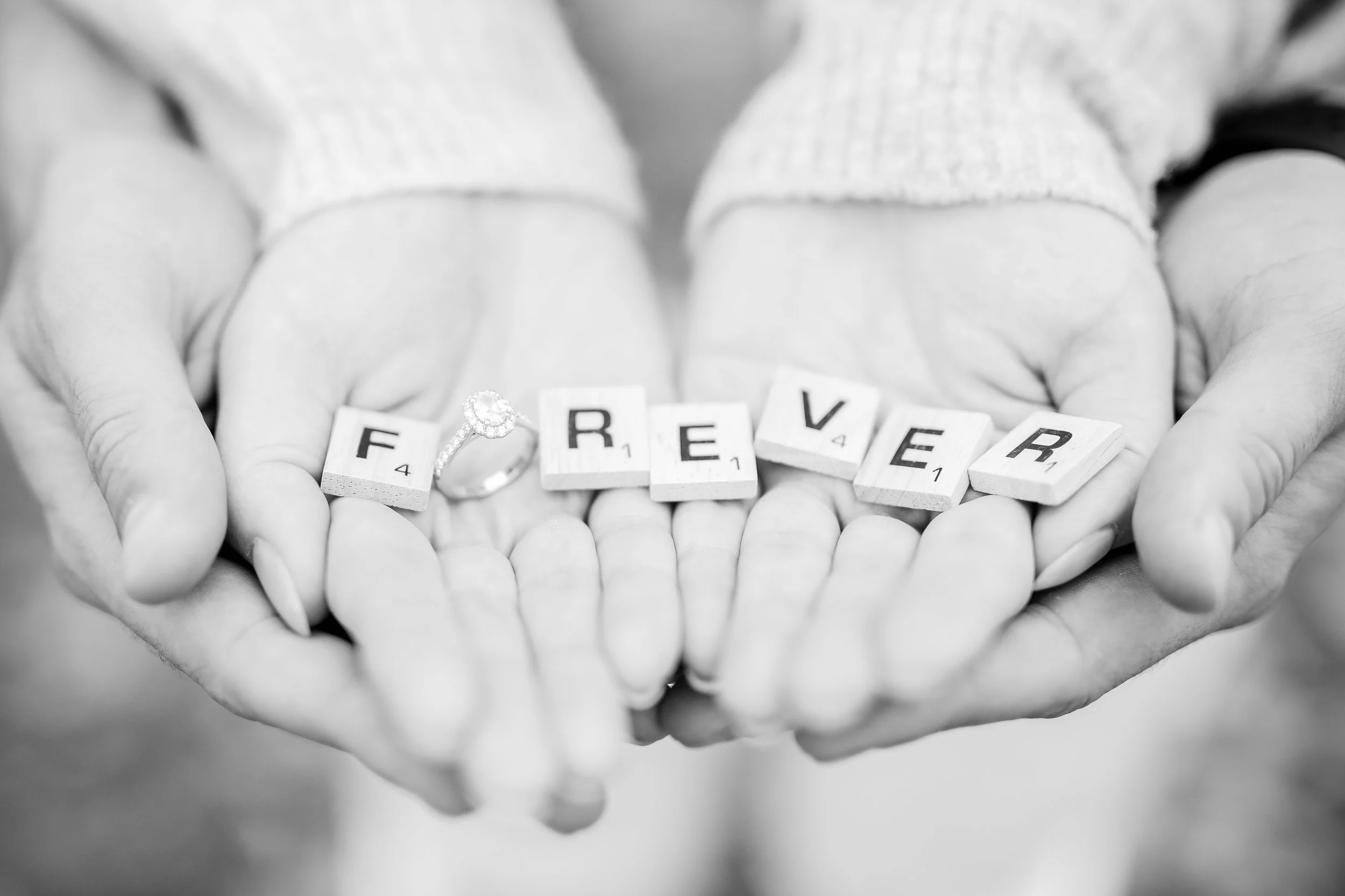 Minnesota wedding photographer, LKW Photography, photographs an engagement session of some close up details.  Here we have hands holding scrabble pieces spelling 'FOREVER' with a ring beside the blocks, black and white photo.