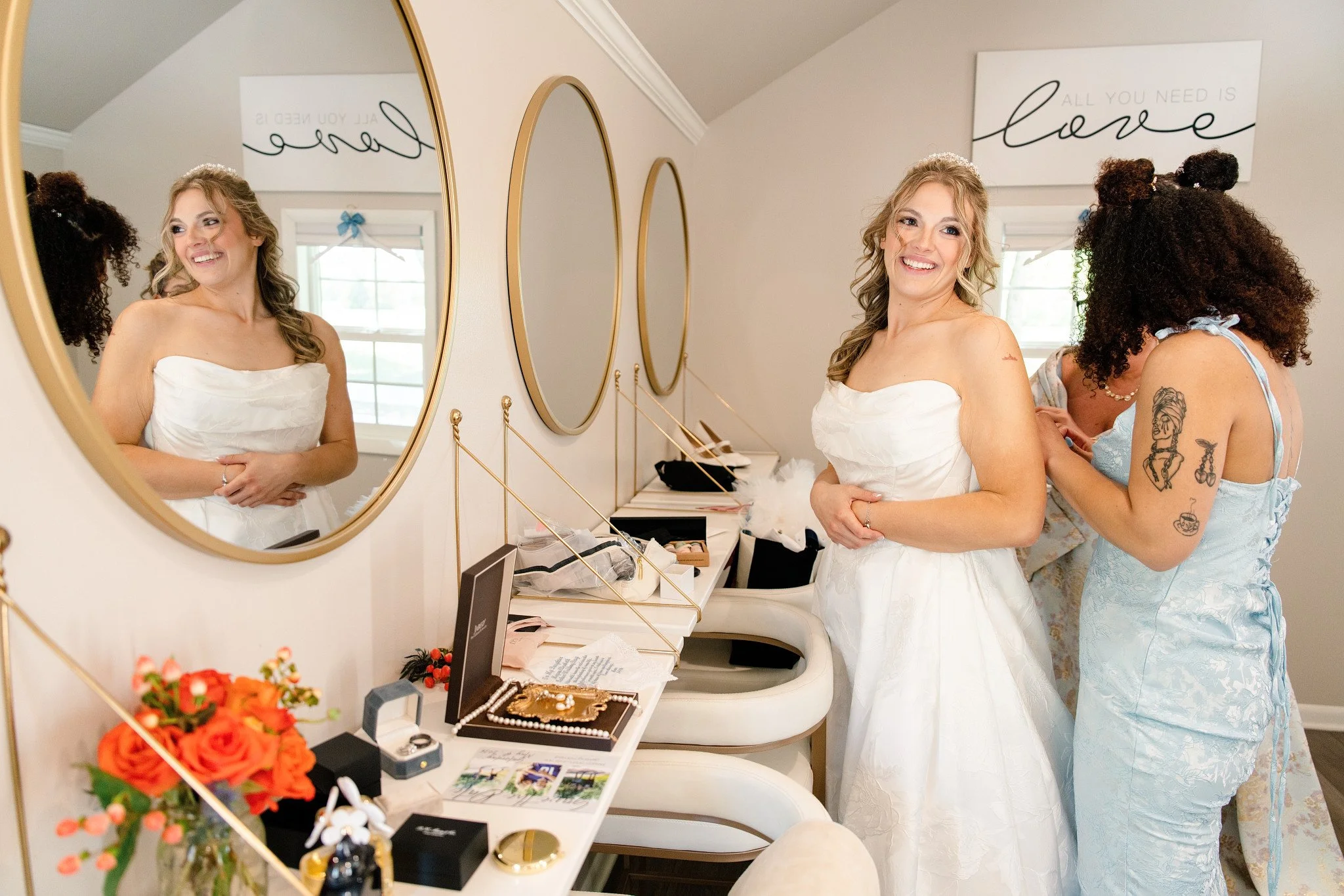 A beautiful bride getting ready with her bridesmaid, and a reflection of her in the mirror.  This showcases the beautiful bride and the bridal suite at Green Acres Events.