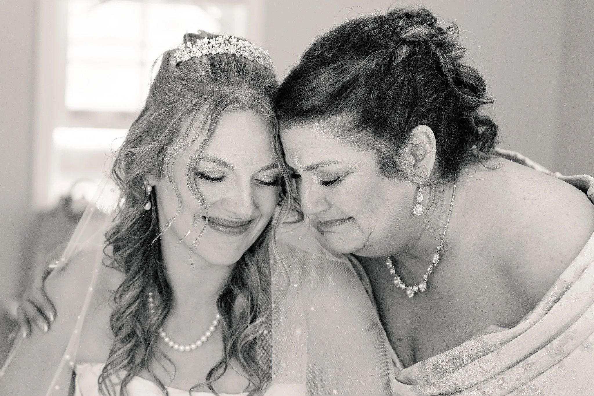 A bride and her mom sharing a moment with a gentle hug and some tears, before heading down the aisle.  Photo is in black and white.