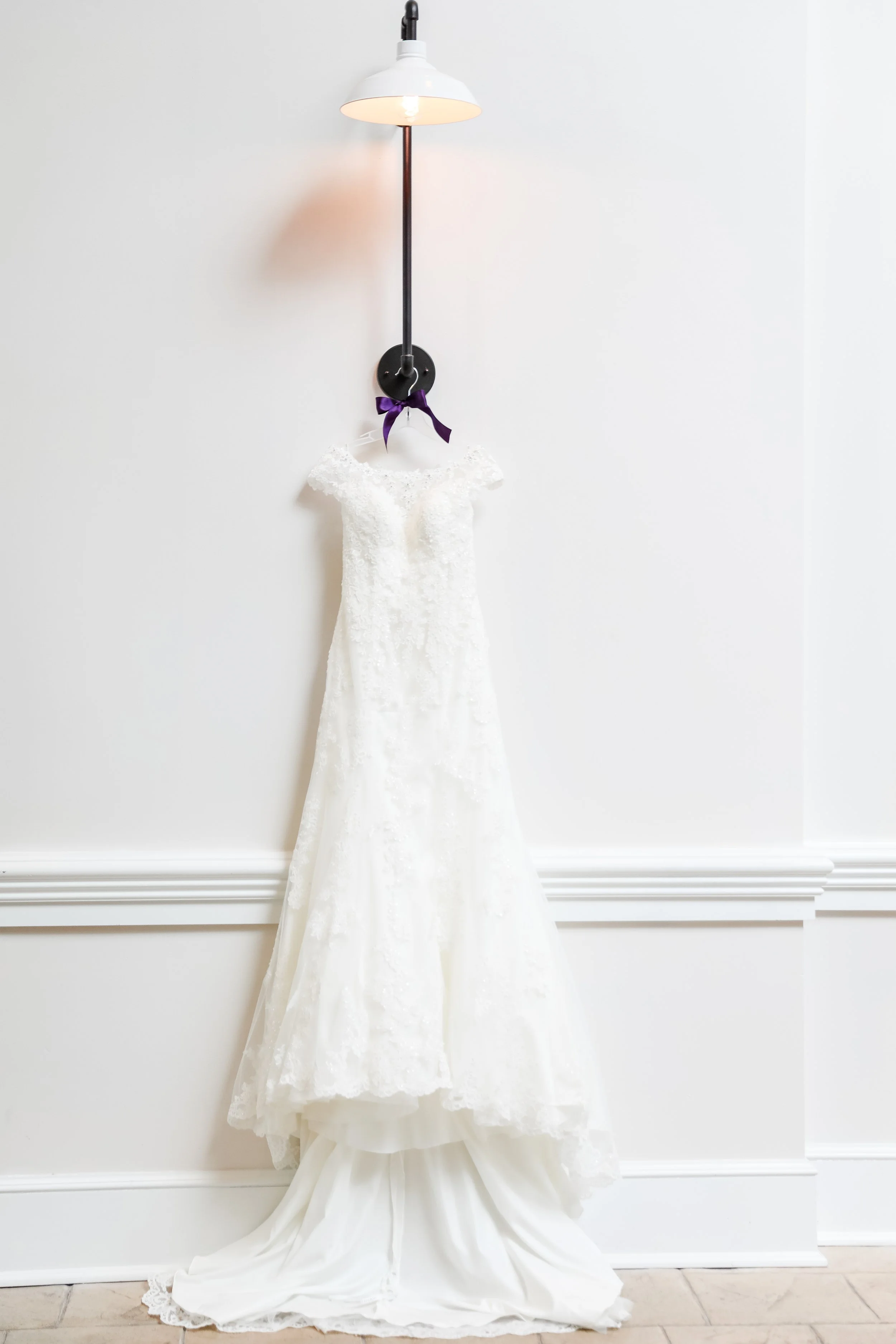 Minnesota based photographer, LKW Photography, photographs a white wedding dress hanging from a wall-mounted light fixture with a purple ribbon tied around it.