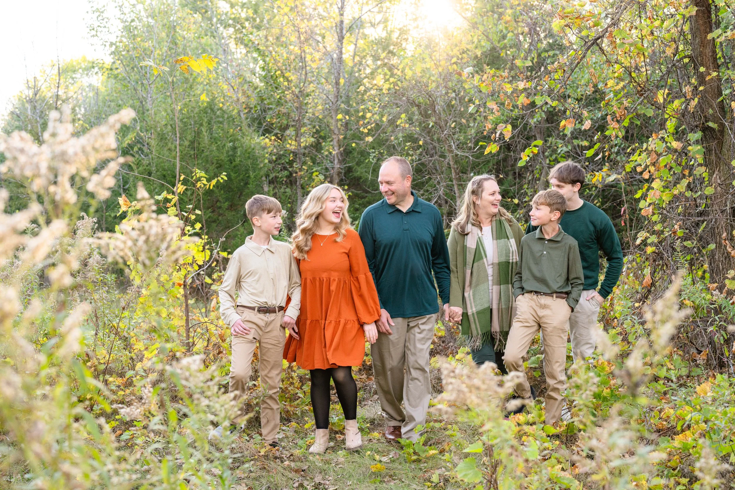 Minnesota portrait photographer, LKW Photography, photographs a family walking outdoors in a wooded area during autumn, holding hands, smiling, and enjoying each other's company.