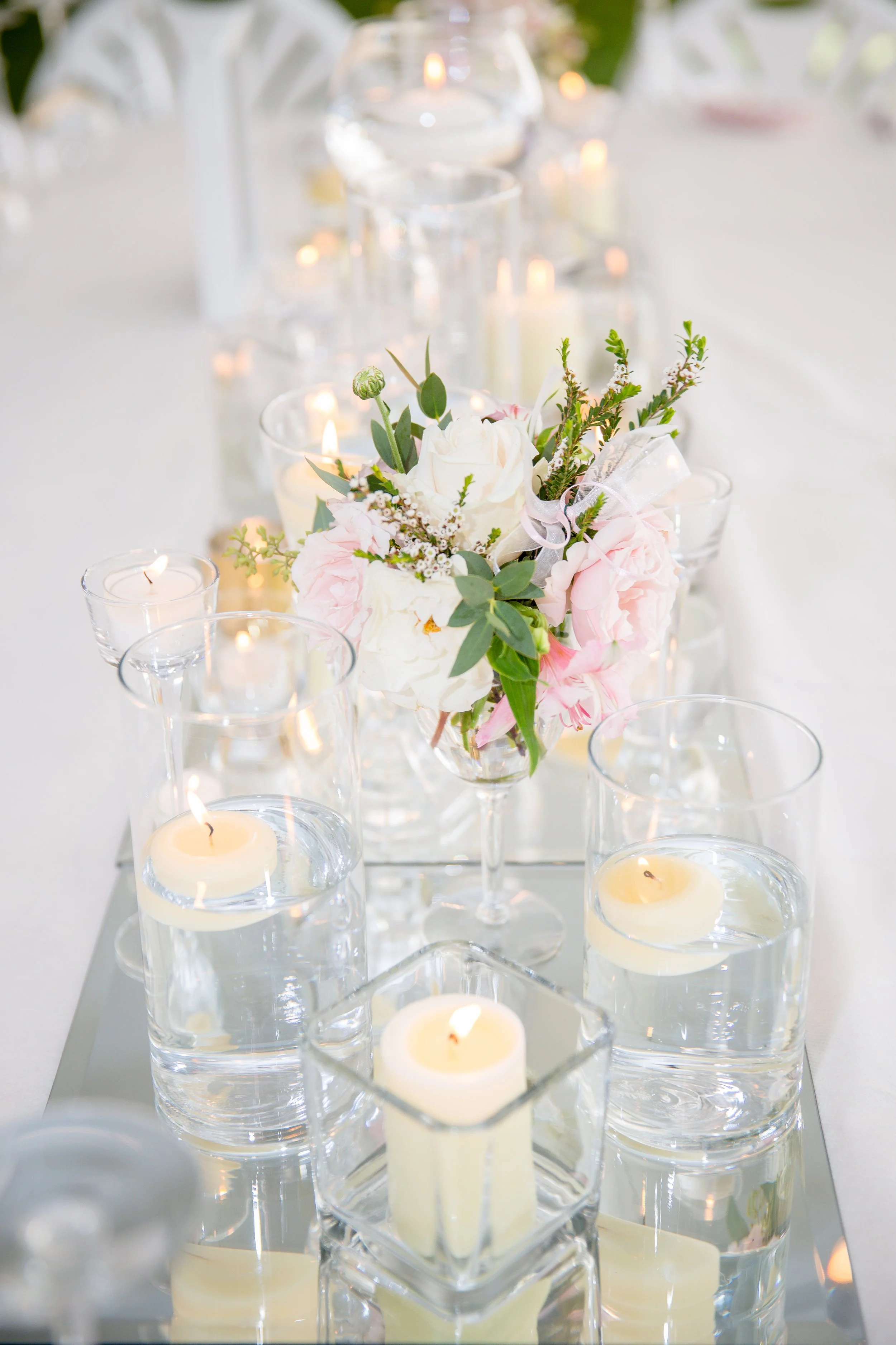 Elegant table centerpiece with pink and white flowers, surrounded by floating candles in glass holders on a mirrored surface at a formal event, photographed by Minnesota based wedding photographer, LKW Photography.