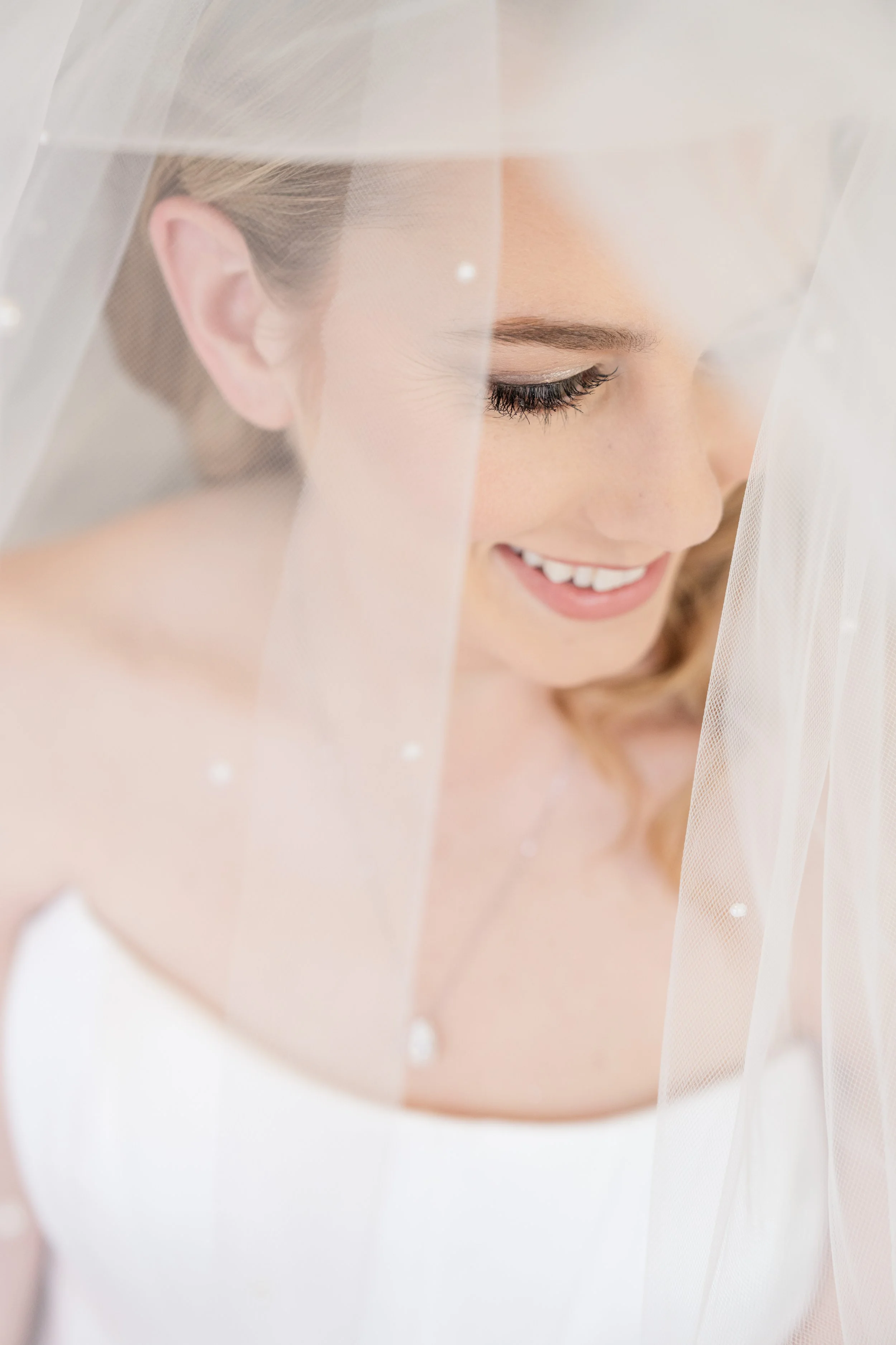 Close-up of a bride smiling softly, partially obscured by a sheer white veil.