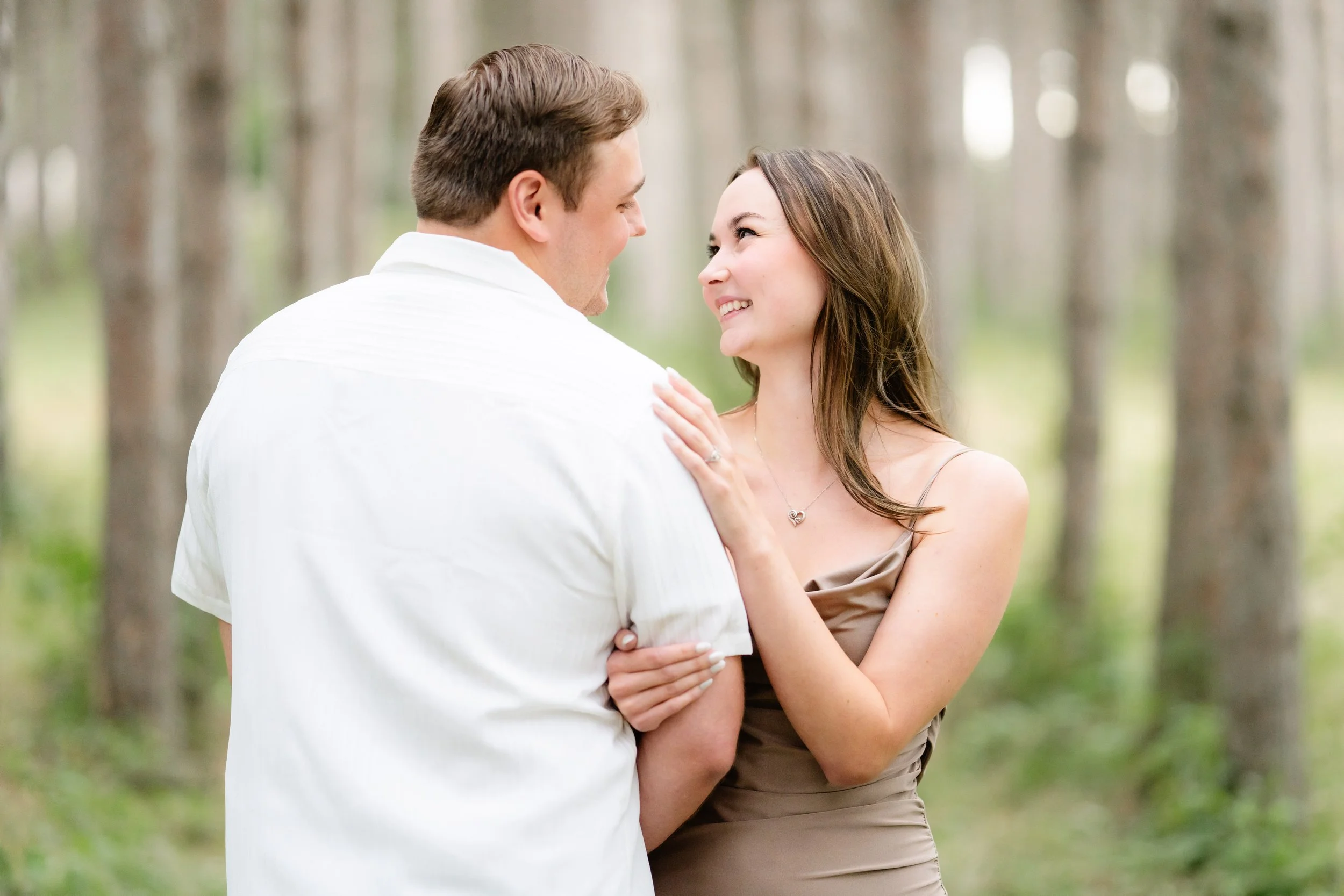 An engaged couple in love embracing in a forest during the daytime, taken by MN photographer LKW Photography.