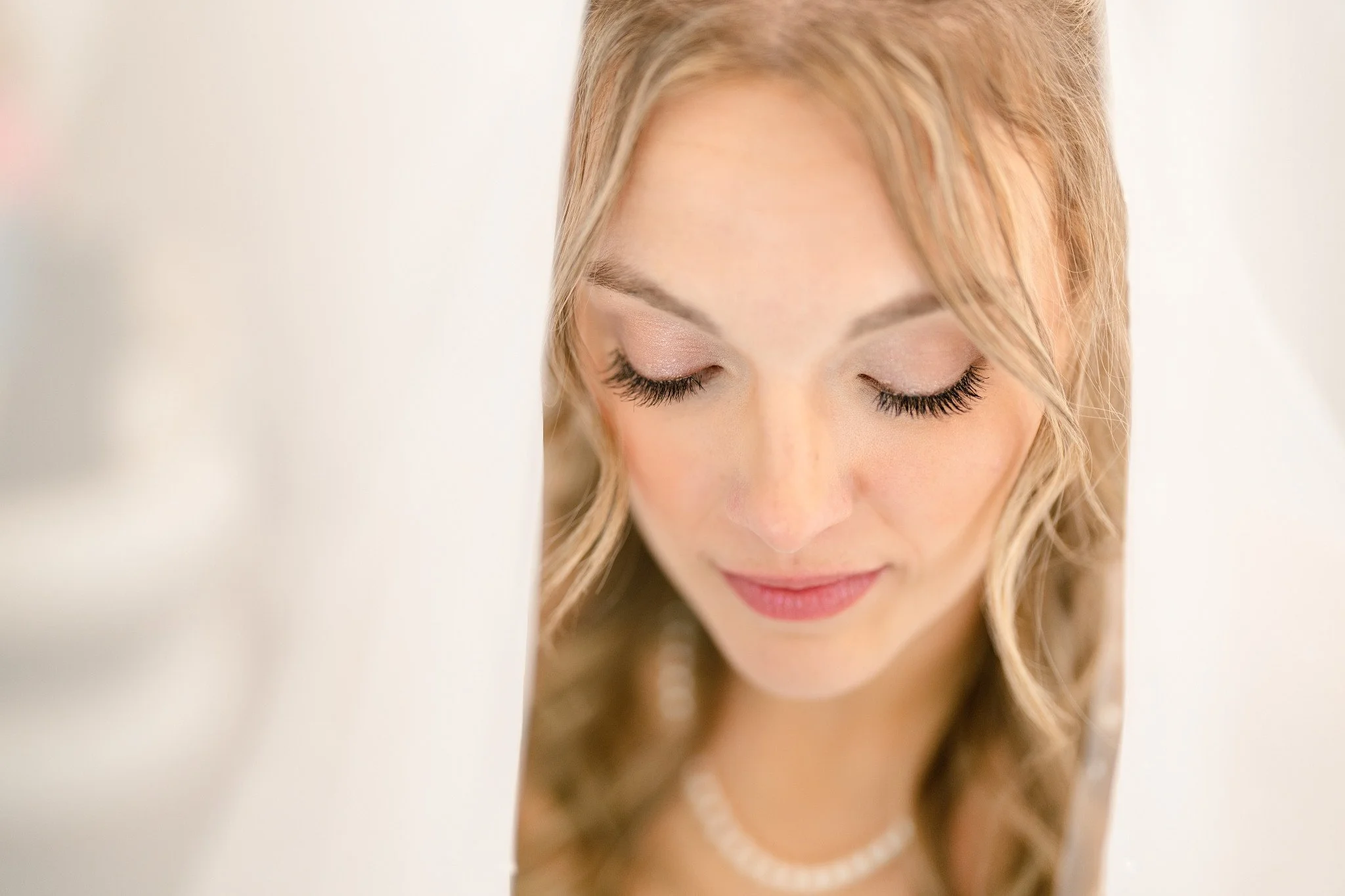 Beauty shot of the bride from under the veil, showcasing her soft glam makeup and pearls.