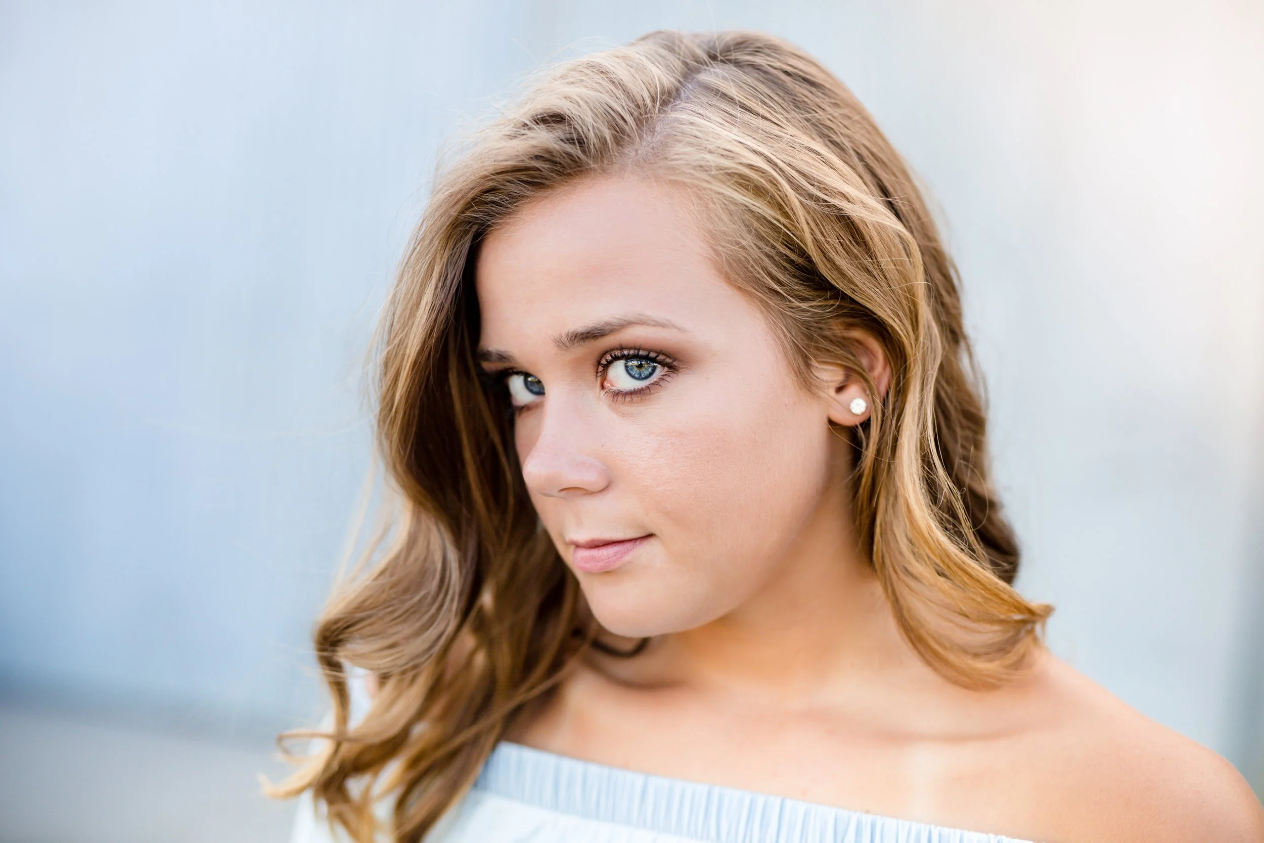 Minnesota senior photographer, LKW Photography, photographs a headshot of a girl with wavy light brown hair and blue eyes, wearing pearl earrings, looking at the camera with a slight smile