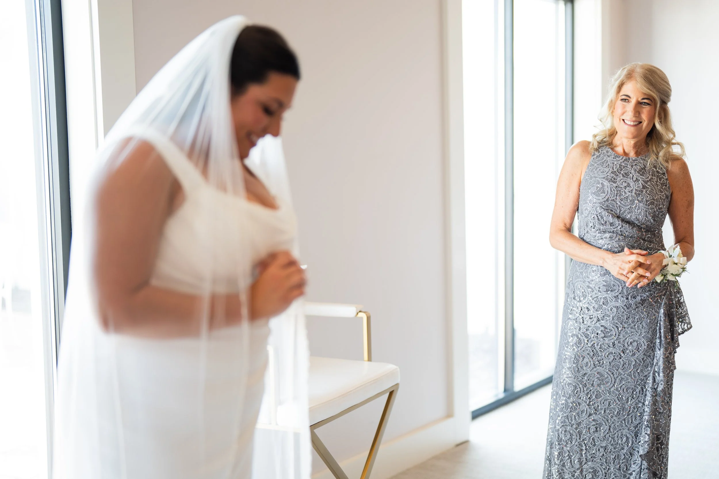 A bride in a white dress with a veil smiling with her head bowed, and her mother looking at her in a reflective moment, taken by MN photographer LKW Photography.