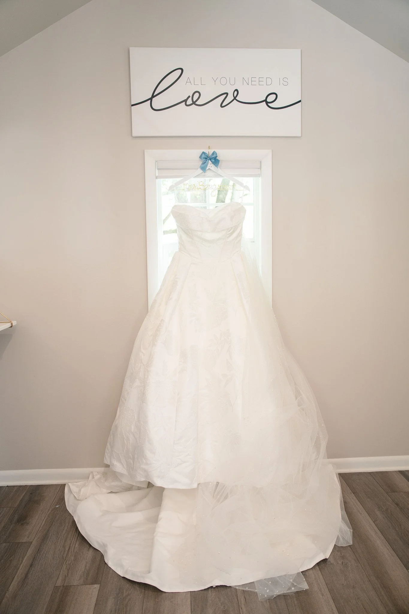 A wedding dress hanging up in front of a window in the bridal suite of Green Acres Events.