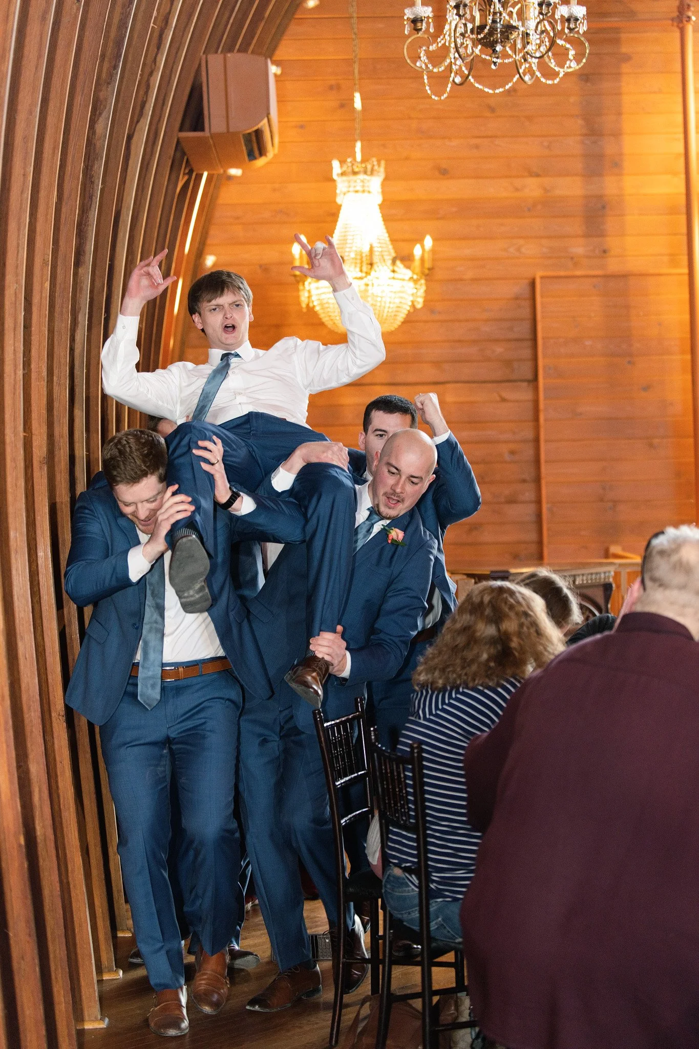 Groomsmen entering for the grand march at a wedding, with 1 groomsmen being carried on the shoulders of 5 other groomsmen.