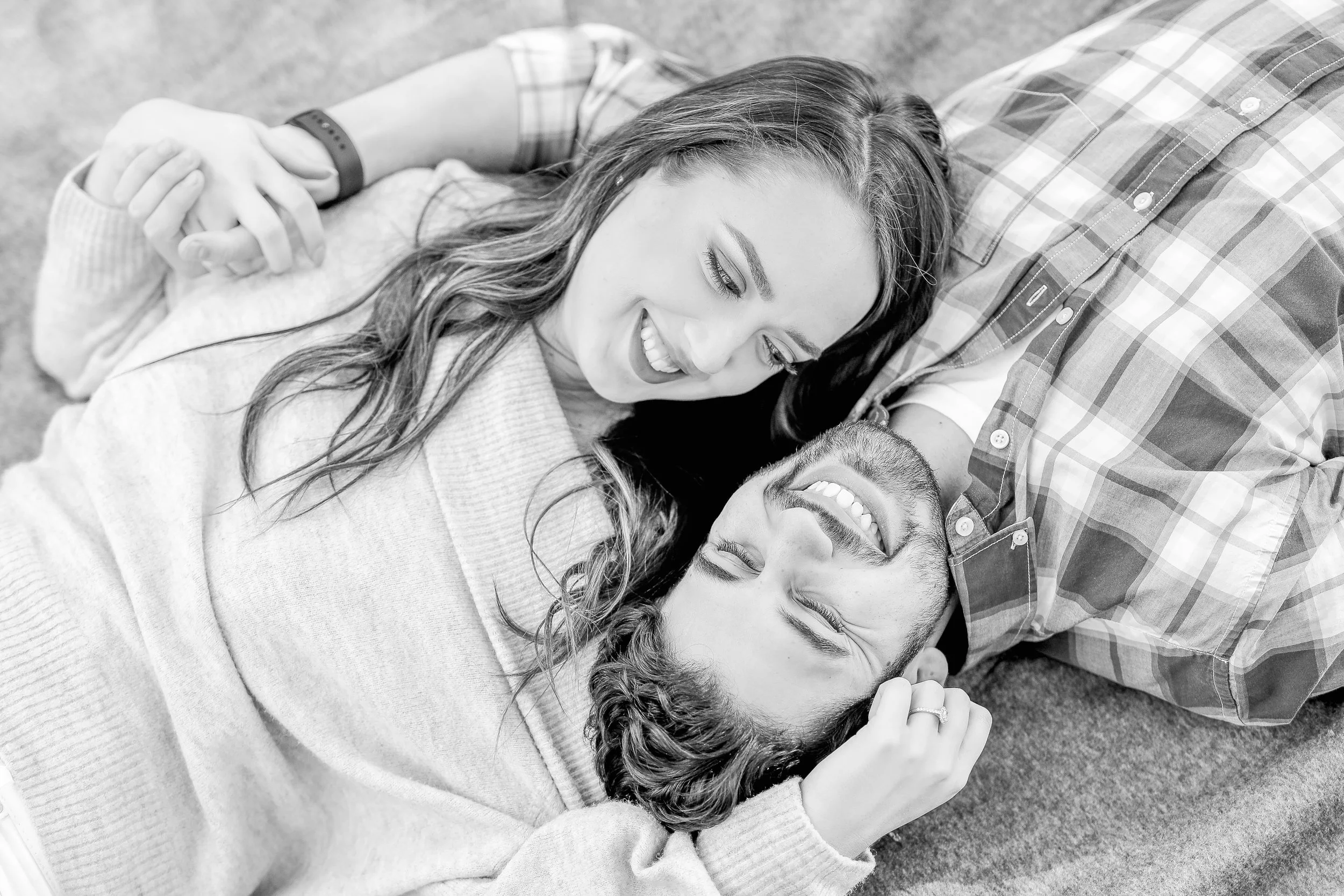 A smiling woman and a man lying on the floor, facing each other and holding hands, sharing a joyful moment, taken by Minnesota based wedding photographer, LKW Photography.