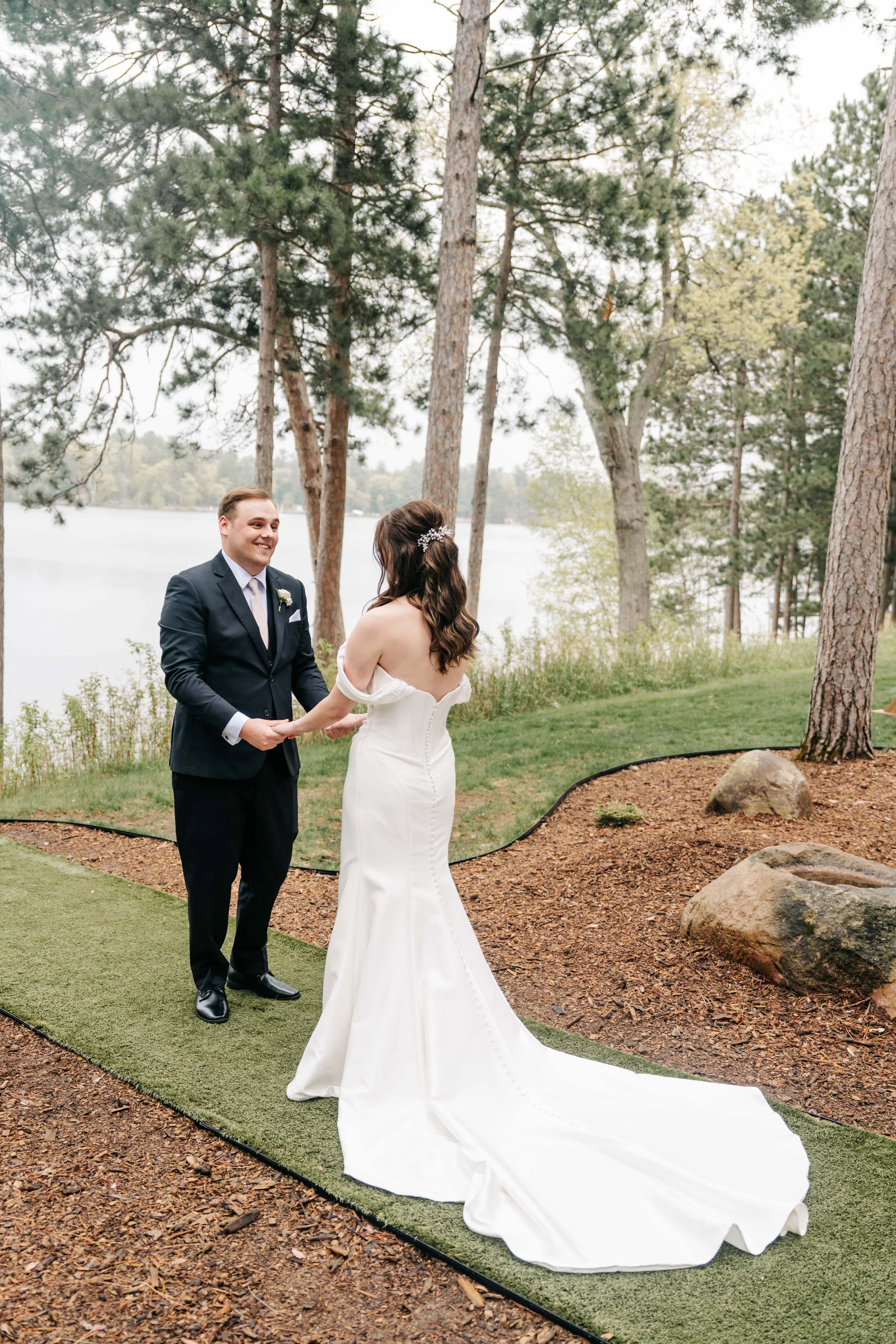 A couple getting married outdoors by a lake, holding hands and facing each other, with trees and water in the background.