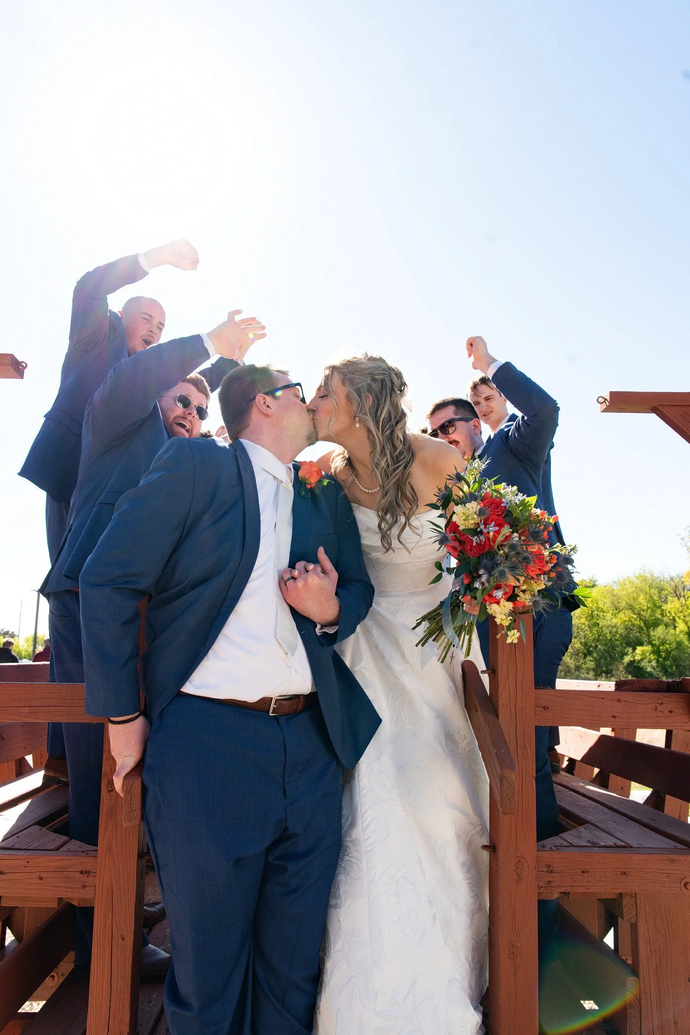 A newlywed couple share a kiss surrounded by their bridal party, on the wagon at Green Acres Events in Eden Prairie, MN.