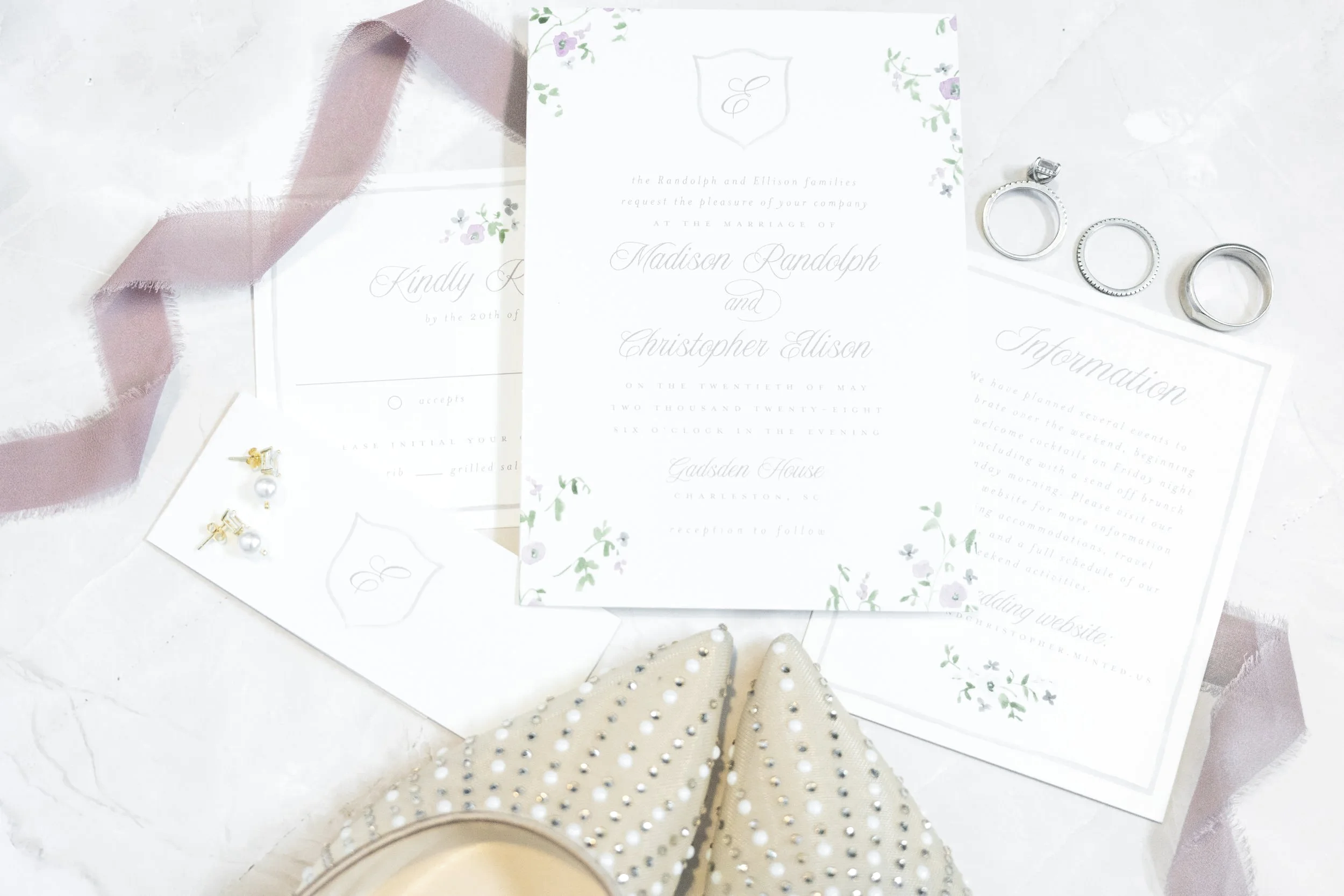 Wedding invitation suite with rings and pearl earrings, on a white surface with a pink ribbon, taken by Minnesota Wedding Photographer LKW Photography.