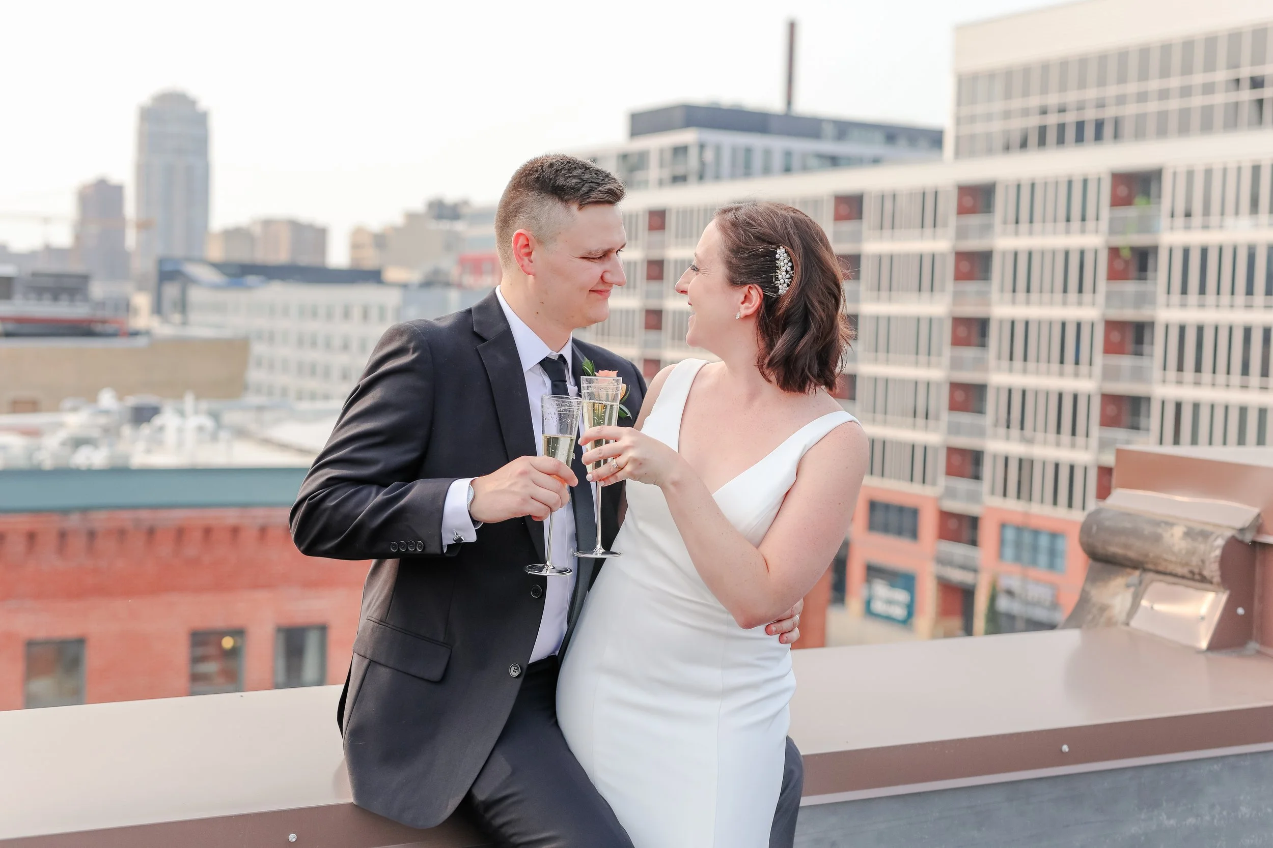 Minnesota based photographer, LKW Photography, photographs a newlywed couple in wedding attire sharing a toast on a city rooftop terrace overlooking Minneapolis.