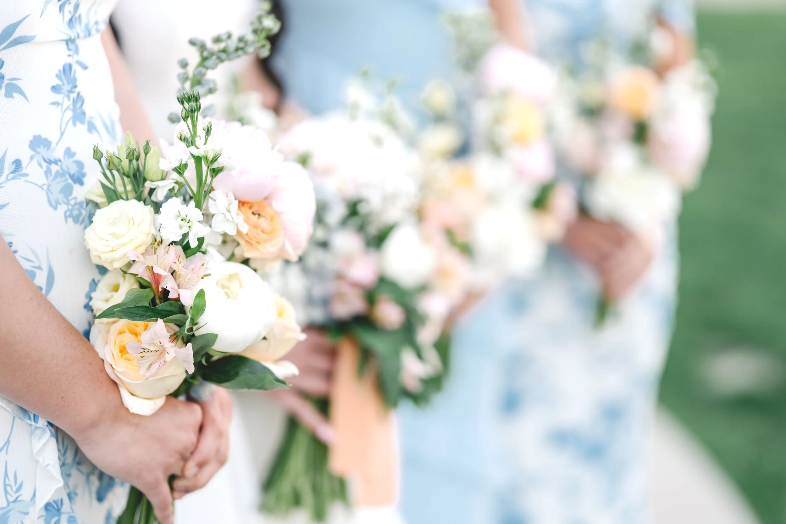 Multiple people standing in a row holding bouquets of flowers, decorated for an outdoor wedding or event.