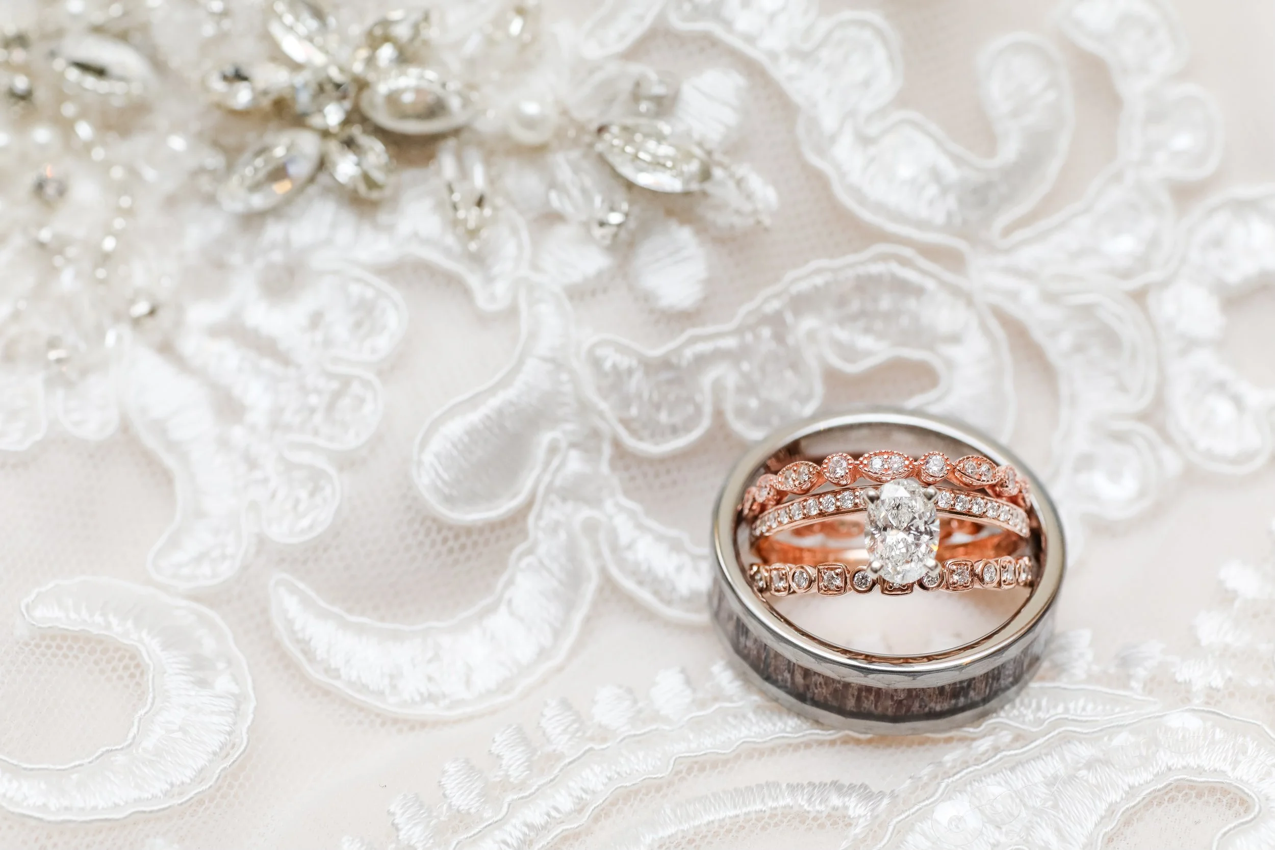 A close-up of a wedding ring set with a diamond engagement ring and matching bands, placed on lacy white fabric, taken by refined Minnesota wedding photographer, LKW Photography.