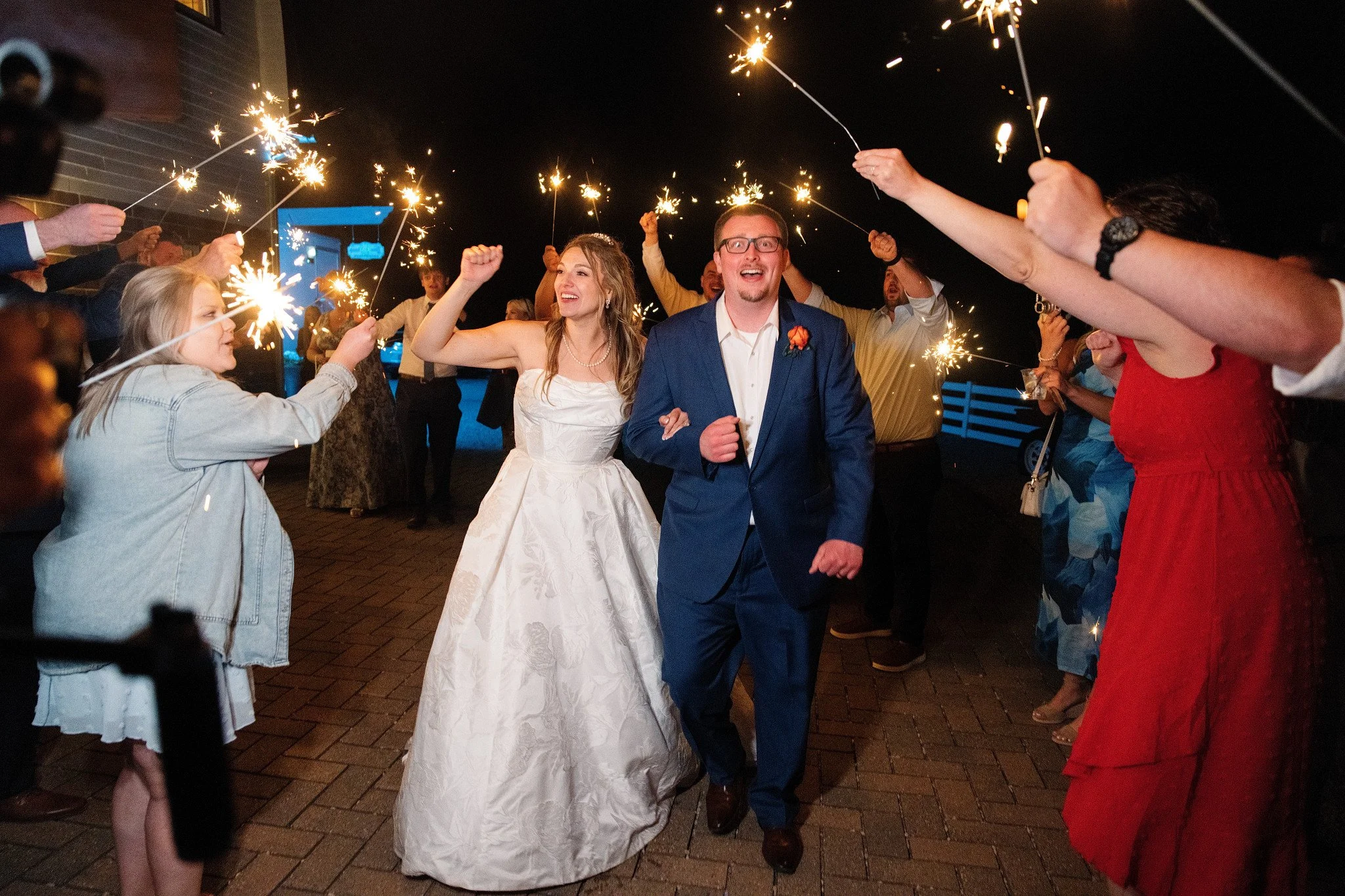 A bride and groom celebrating at night with sparklers surrounded by friends and family.