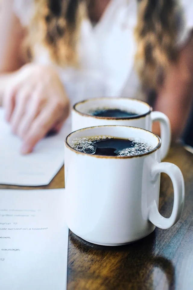 A woman studying a menu with two cups of coffee on the table, illustrating the nervous system freeze of an underfunctioner faced with too many choices.