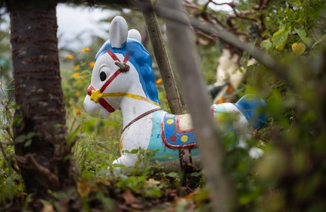 An empty playground rocking horse beneath trees, representing how childhood experiences and unconscious patterns continue to shape adult relationships and conflict.