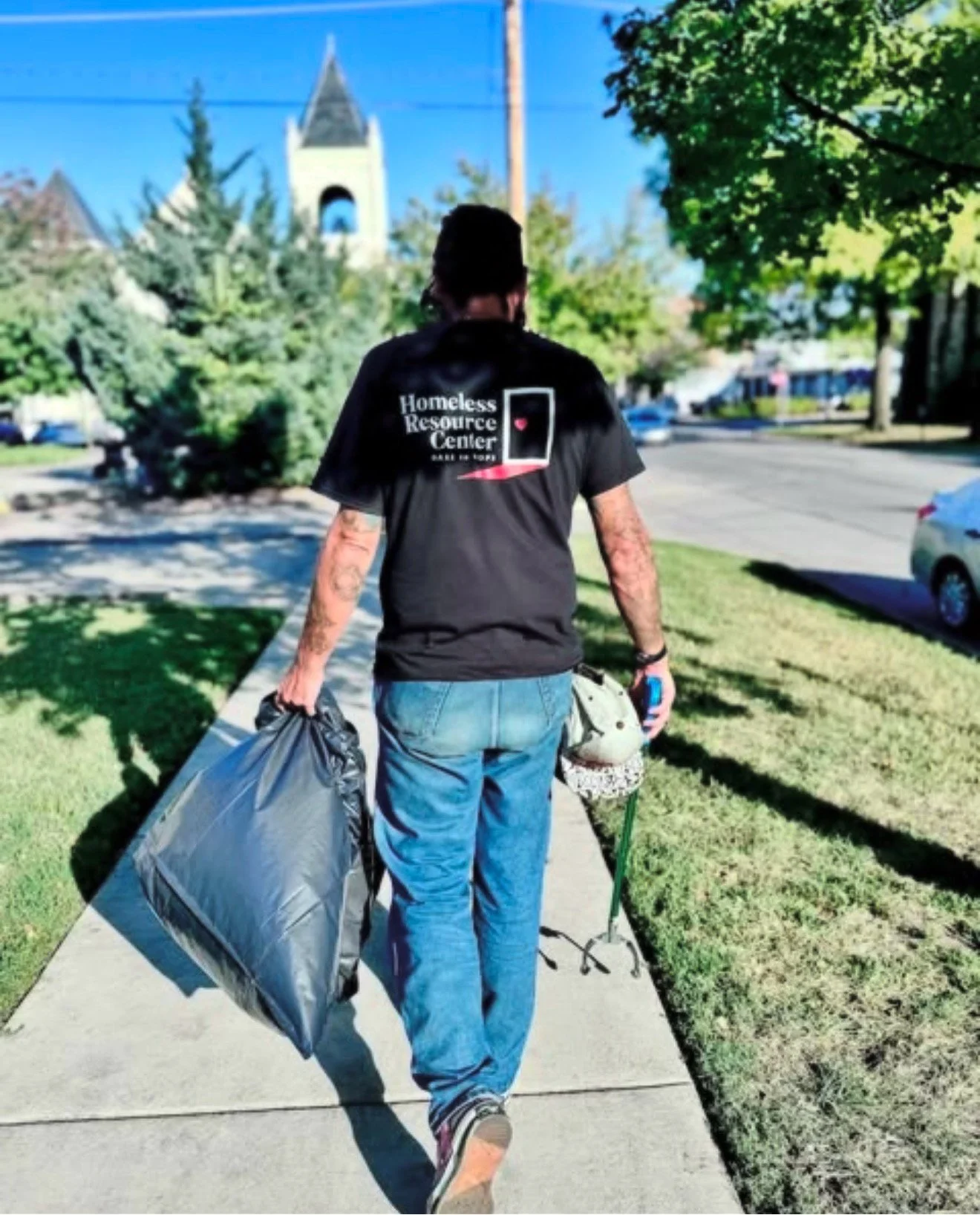 A Job Empowerment worker in an HRC shirt carrying a full trash bag down a Lawrence sidewalk