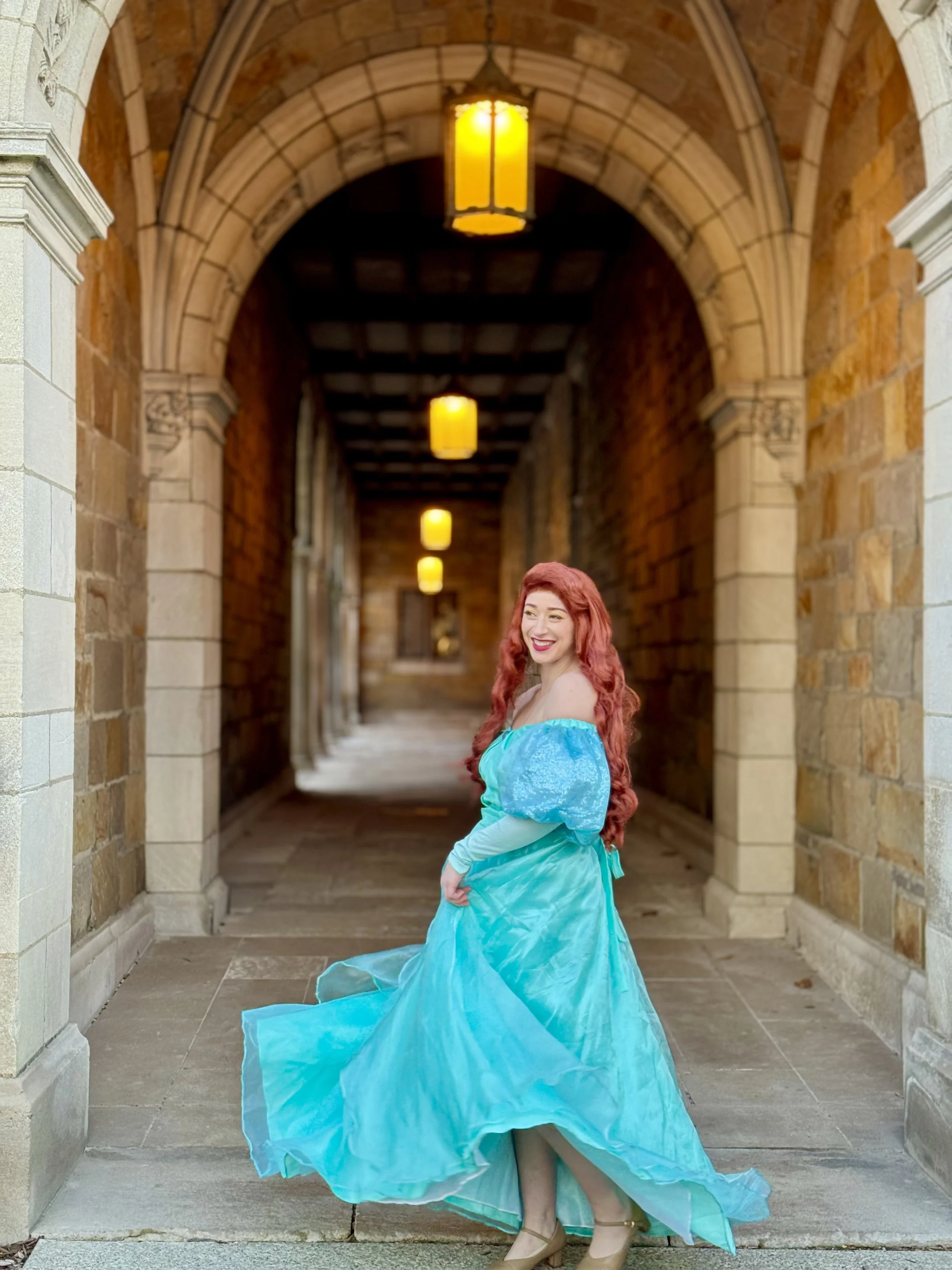 Person dressed as a fairy tale character with red hair and a turquoise dress sitting outdoors. Ariel face character, face character, princess birthday party, princess party in Michigan, Ariel for hire, mermaid party

