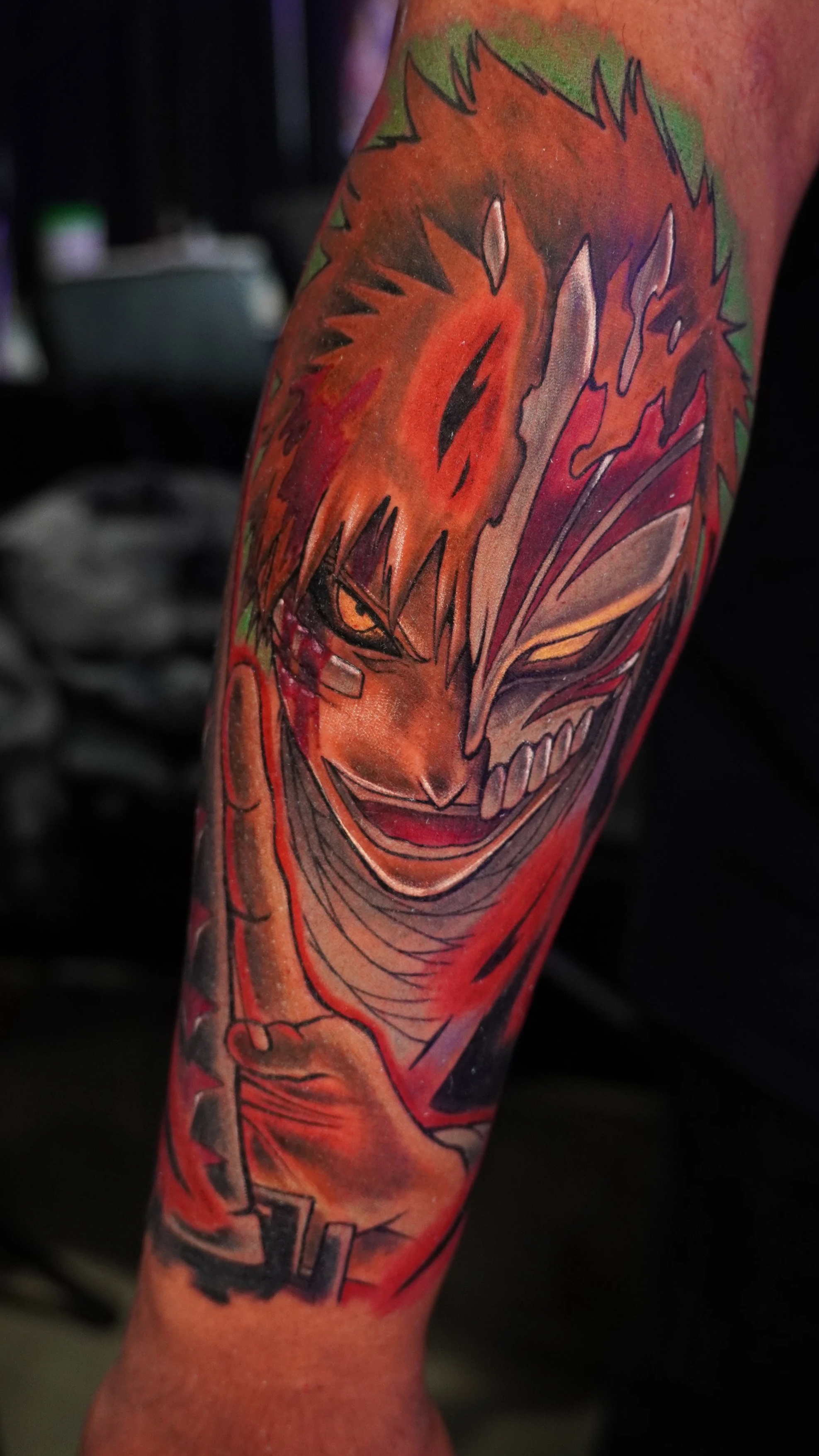 A colorful tattoo featuring a fierce, stylized anime character with spiky hair, sharp teeth, and an intense expression, on someone's arm.