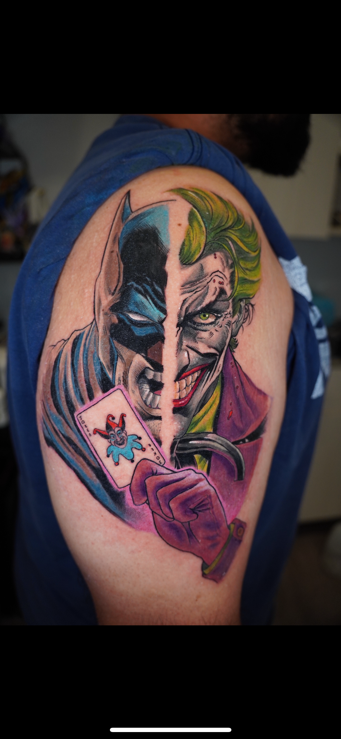 Tattoo of Batman's face split with Joker's face on a person's upper arm.