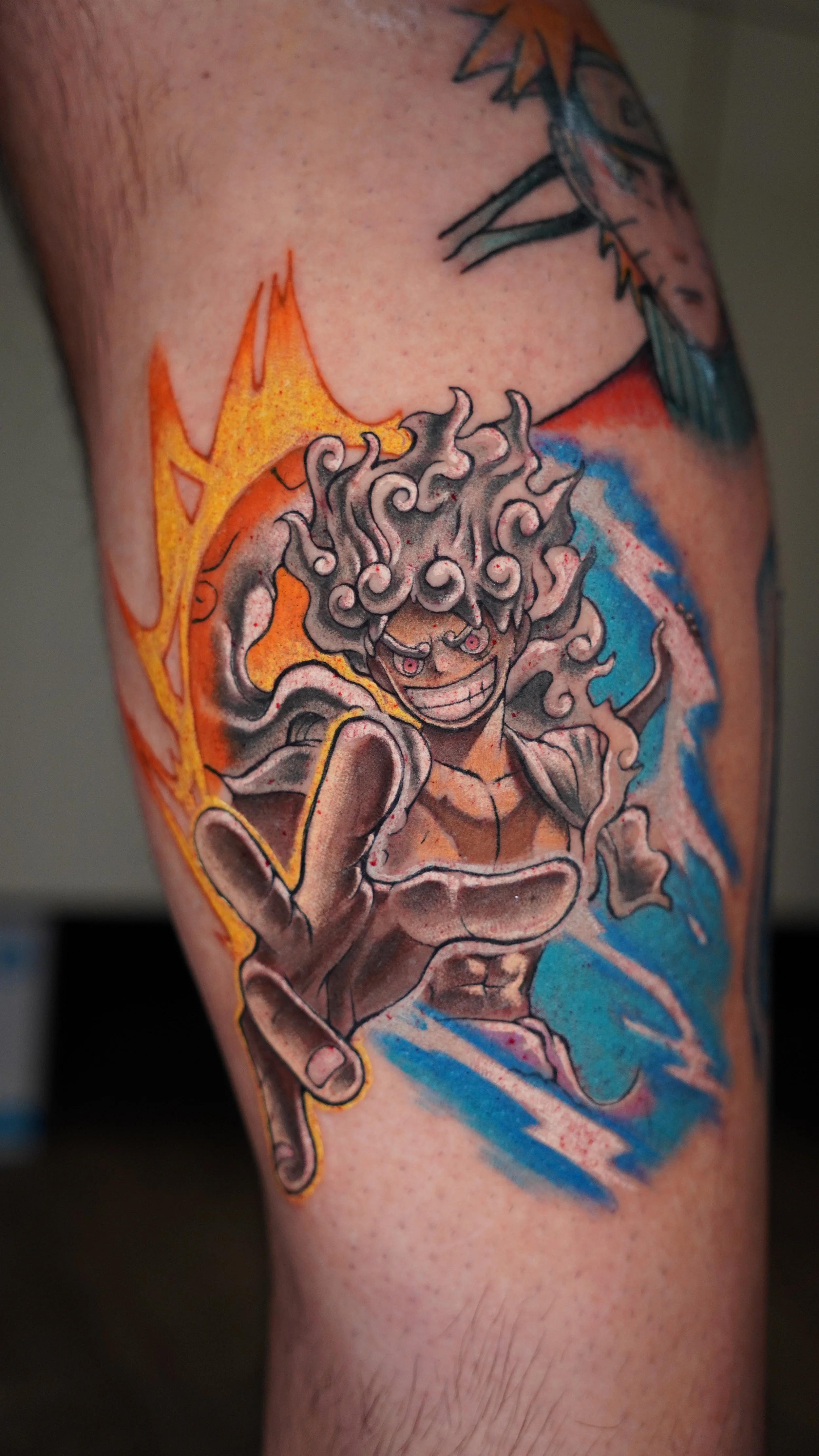Tattoo of a colorful Luffy with wild hair, smiling and holding out his hand, surrounded by blue and orange background elements.