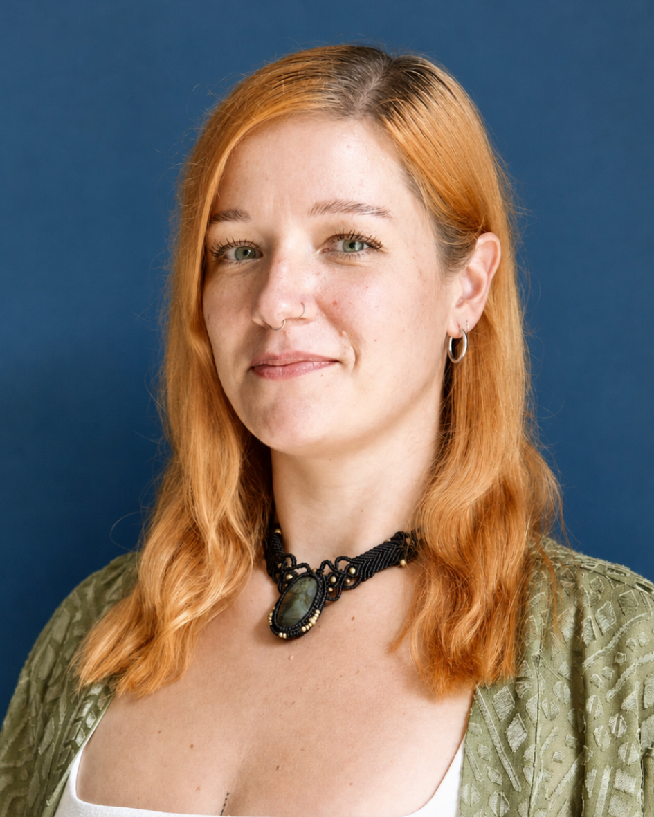 Portrait of Sarah with shoulder-length red hair, wearing a green top and pendant necklace against a blue background.