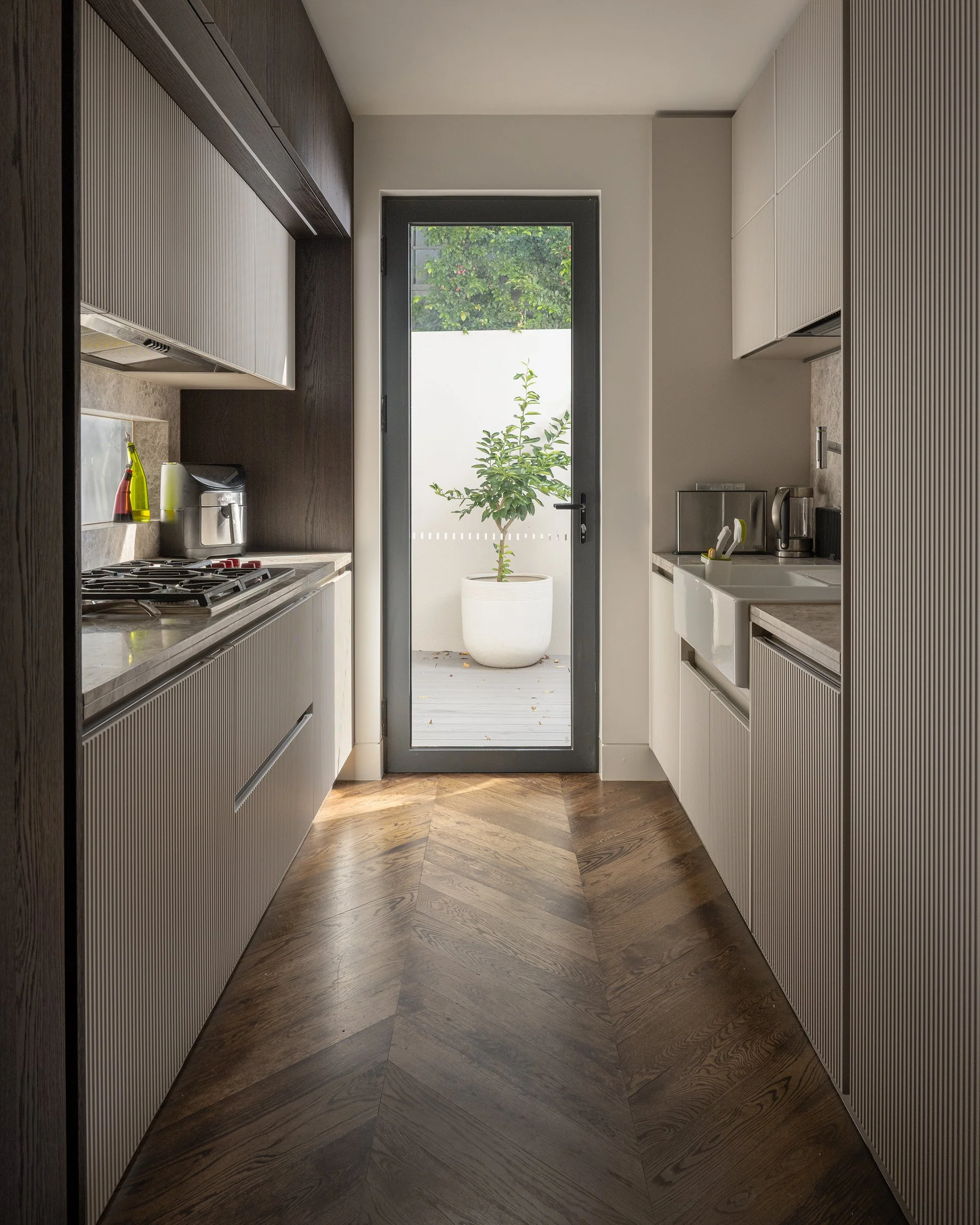Modern kitchen with white and dark wood cabinets, a glass door opening to a small outdoor patio with a potted plant.
