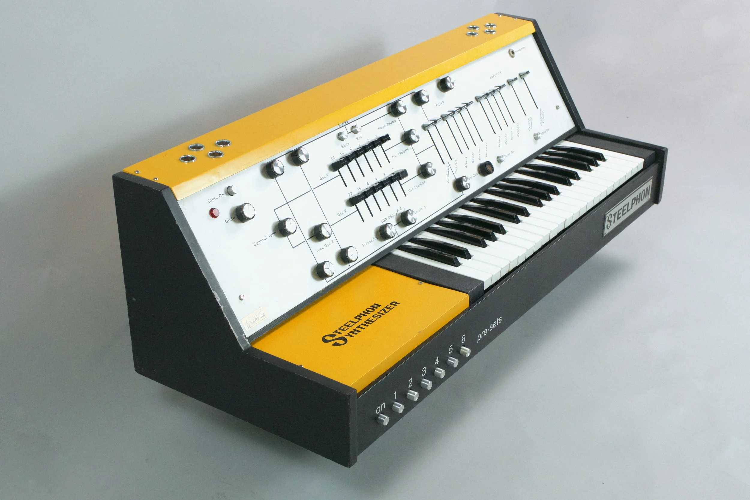 This is  a specimen of the very early production run - a handful of yellow units with metal control panels - much more rare than the wooden version. The synths are identical electronically but use different key beds. 