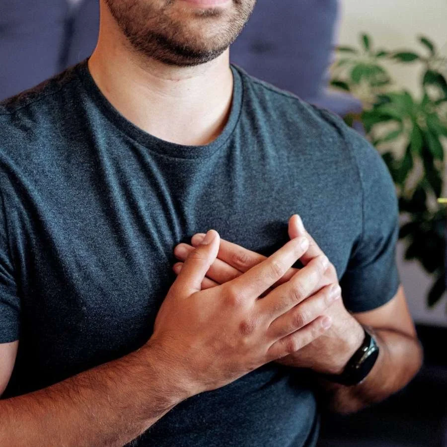 A man wearing a dark blue t-shirt holds his hands over his chest